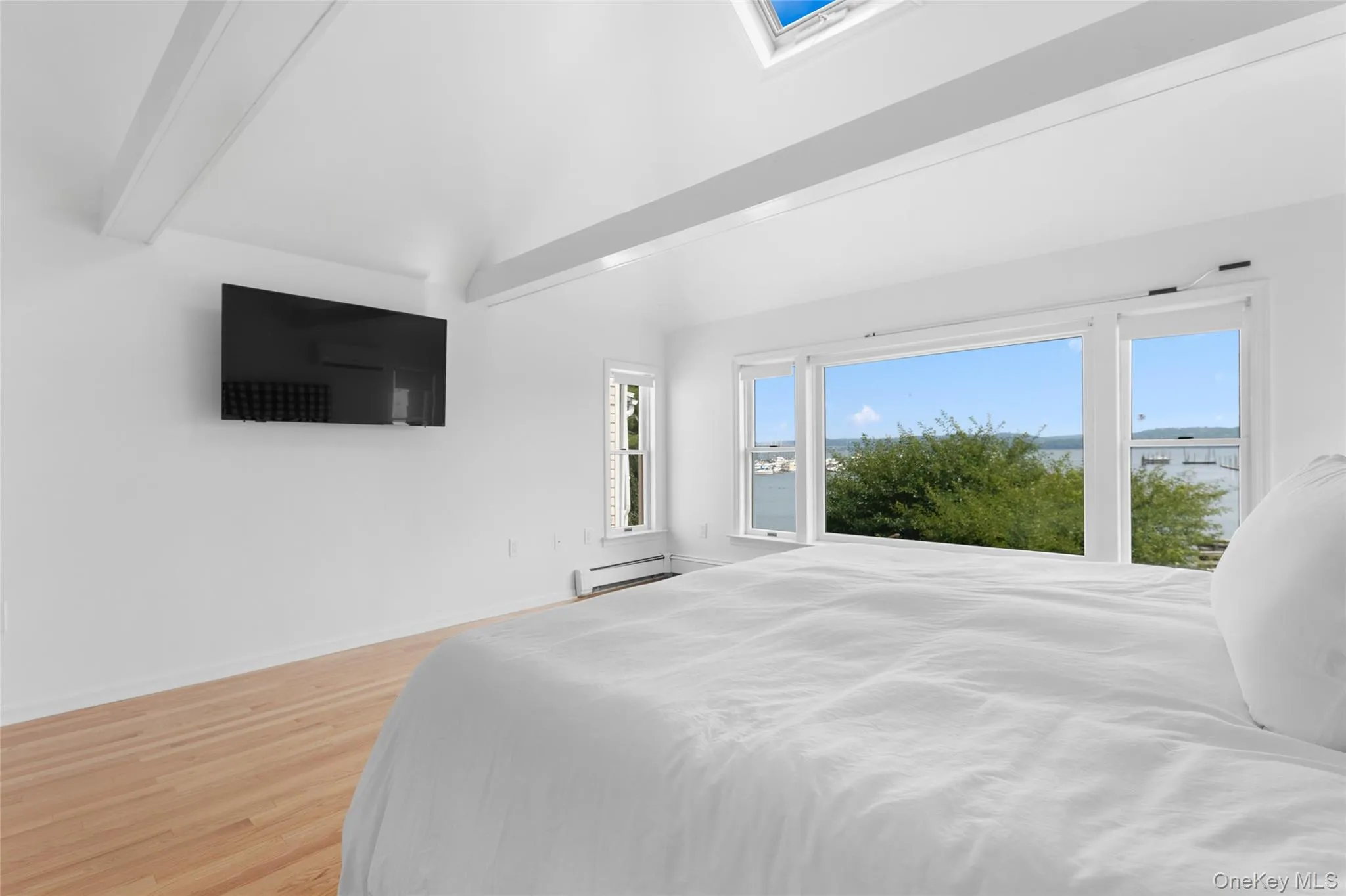 Bedroom with beamed ceiling, light wood-style flooring, and a baseboard radiator Bedroom with beamed ceiling, light wood-style flooring, and a baseboard radiator