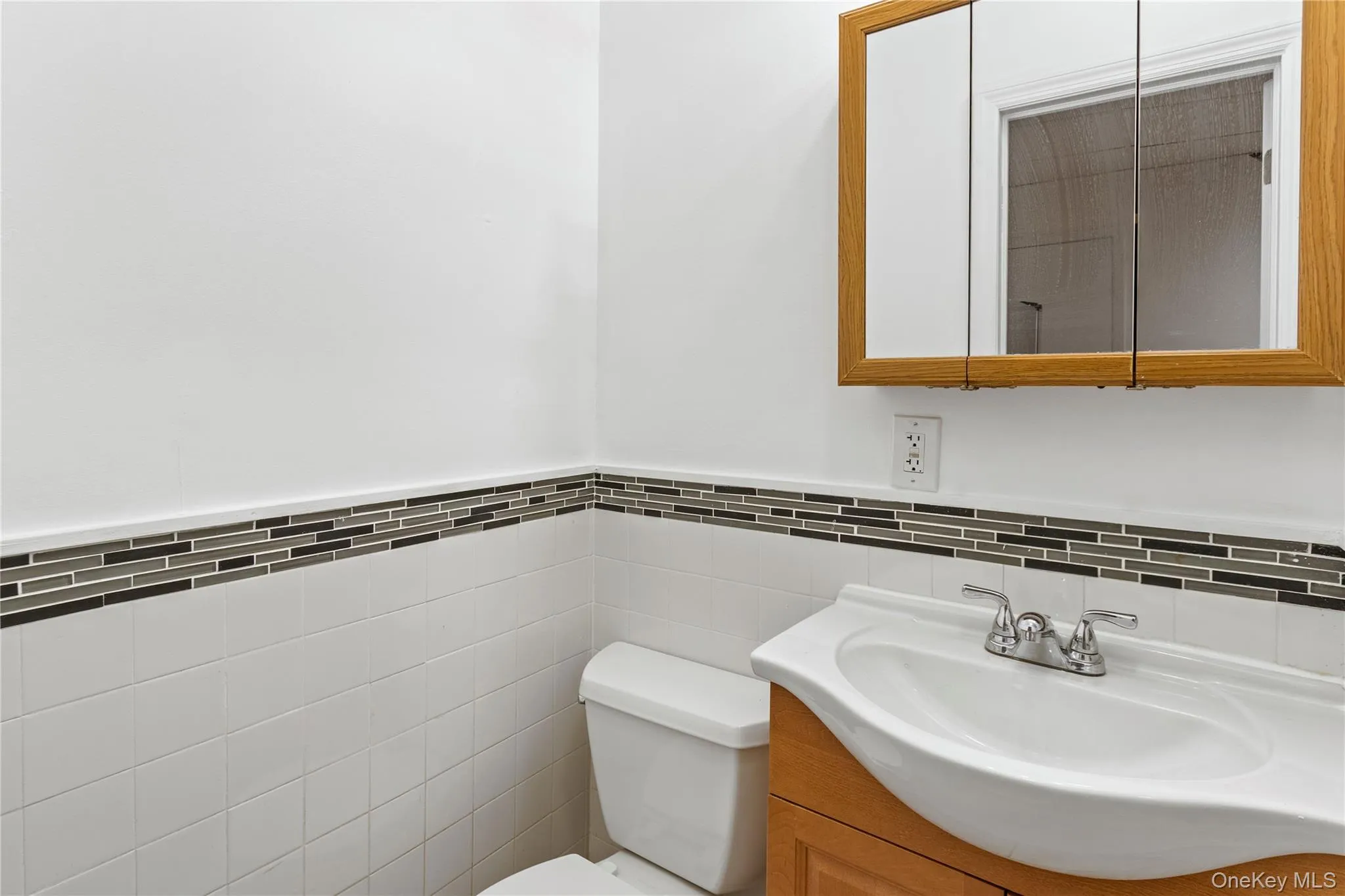 Half bath featuring vanity, tile walls, and a wainscoted wall Half bath featuring vanity, tile walls, and a wainscoted wall