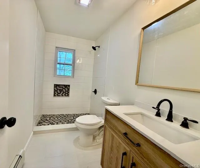 Bathroom featuring vanity, a baseboard radiator, a shower stall, and light tile patterned floors Bathroom featuring vanity, a baseboard radiator, a shower stall, and light tile patterned floors