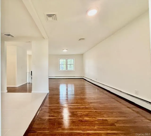 Empty room featuring dark wood-style floors and a baseboard heating unit Empty room featuring dark wood-style floors and a baseboard heating unit