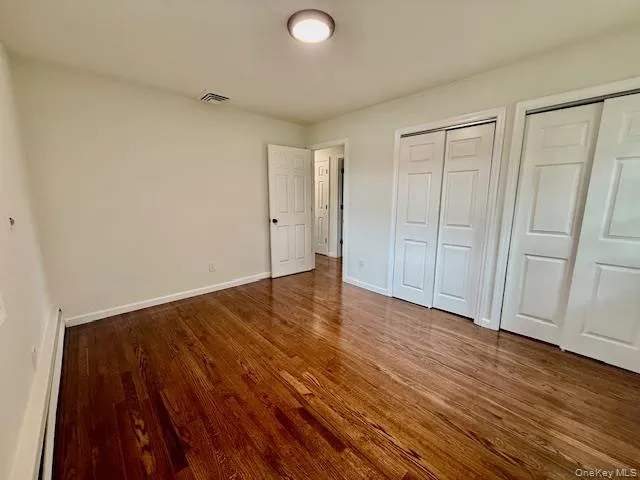 Unfurnished bedroom featuring two closets, a baseboard radiator, and wood finished floors Unfurnished bedroom featuring two closets, a baseboard radiator, and wood finished floors