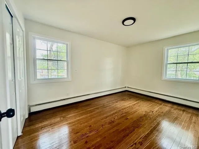 Unfurnished bedroom featuring hardwood / wood-style floors, a baseboard heating unit, and a closet Unfurnished bedroom featuring hardwood / wood-style floors, a baseboard heating unit, and a closet