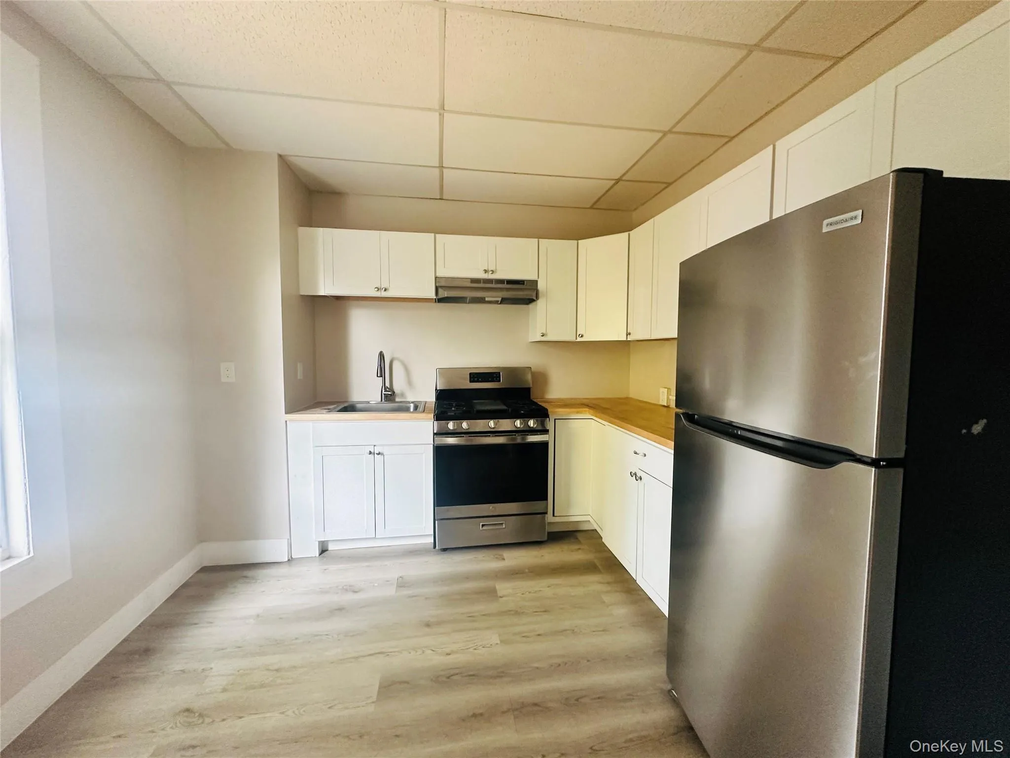 Kitchen featuring appliances with stainless steel finishes, a paneled ceiling, white cabinets, light countertops, and light wood-style flooring Kitchen featuring appliances with stainless steel finishes, a paneled ceiling, white cabinets, light countertops, and light wood-style flooring