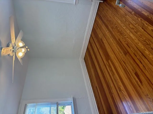 Empty room with a textured wall, wood finished floors, and a ceiling fan Empty room with a textured wall, wood finished floors, and a ceiling fan