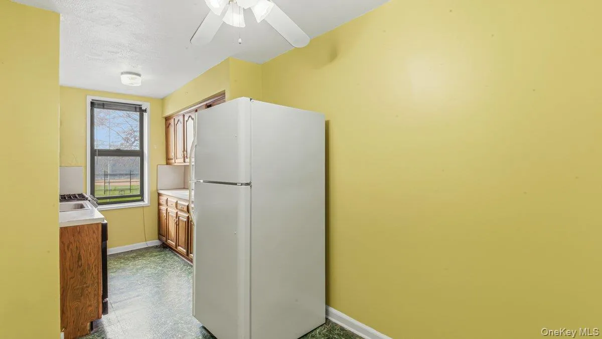 Kitchen with freestanding refrigerator, light countertops, a ceiling fan, and brown cabinets Kitchen with freestanding refrigerator, light countertops, a ceiling fan, and brown cabinets