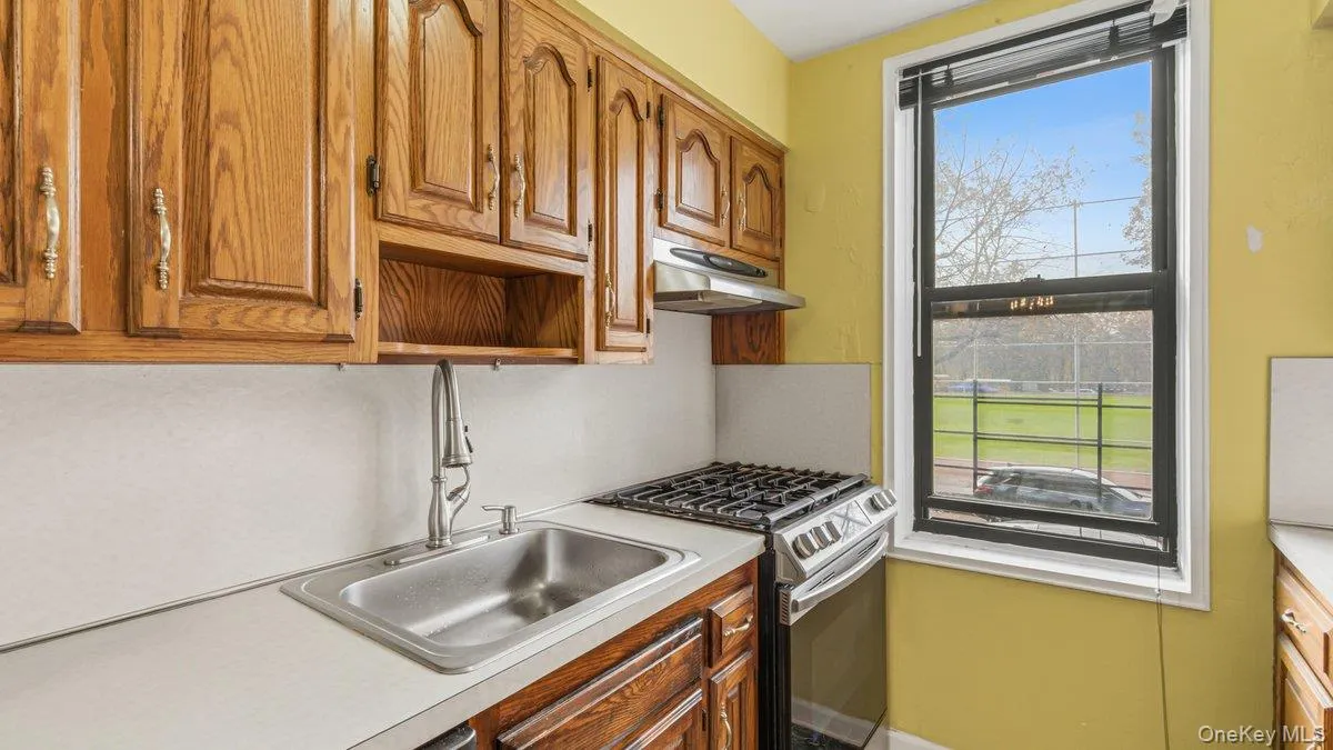 Kitchen featuring gas stove, light countertops, open shelves, brown cabinetry, and under cabinet range hood Kitchen featuring gas stove, light countertops, open shelves, brown cabinetry, and under cabinet range hood