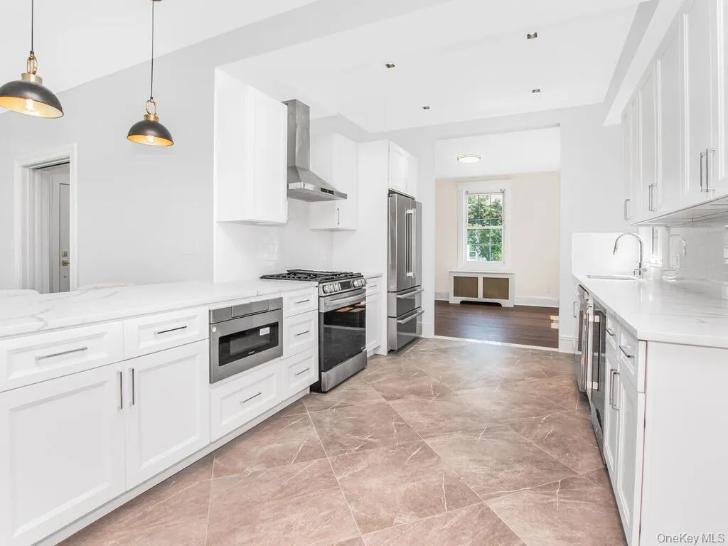 Kitchen with appliances with stainless steel finishes, wall chimney exhaust hood, light stone counters, white cabinets, and radiator Kitchen with appliances with stainless steel finishes, wall chimney exhaust hood, light stone counters, white cabinets, and radiator