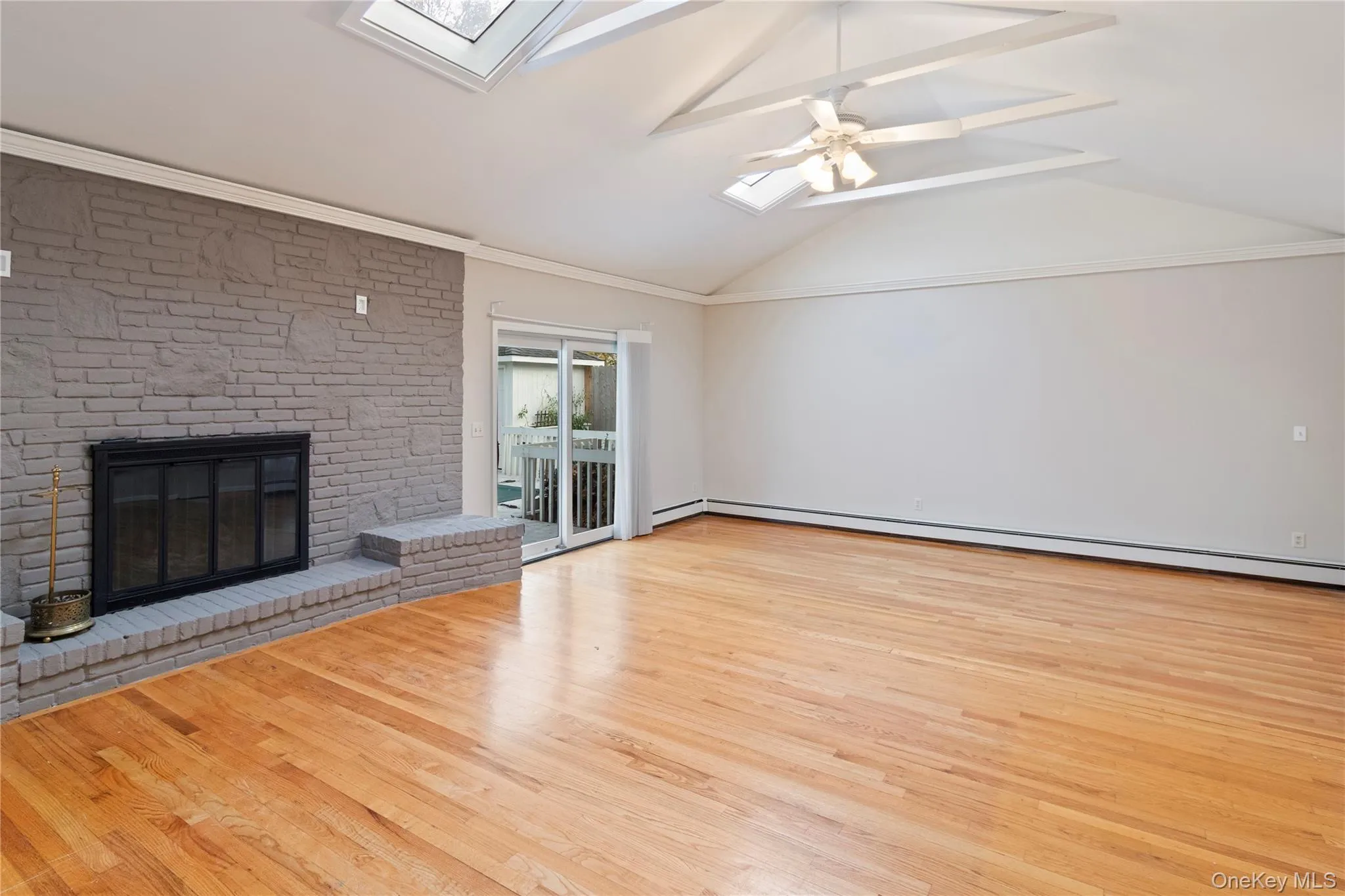Unfurnished living room with a skylight, wood finished floors, a brick fireplace, and baseboard heating Unfurnished living room with a skylight, wood finished floors, a brick fireplace, and baseboard heating
