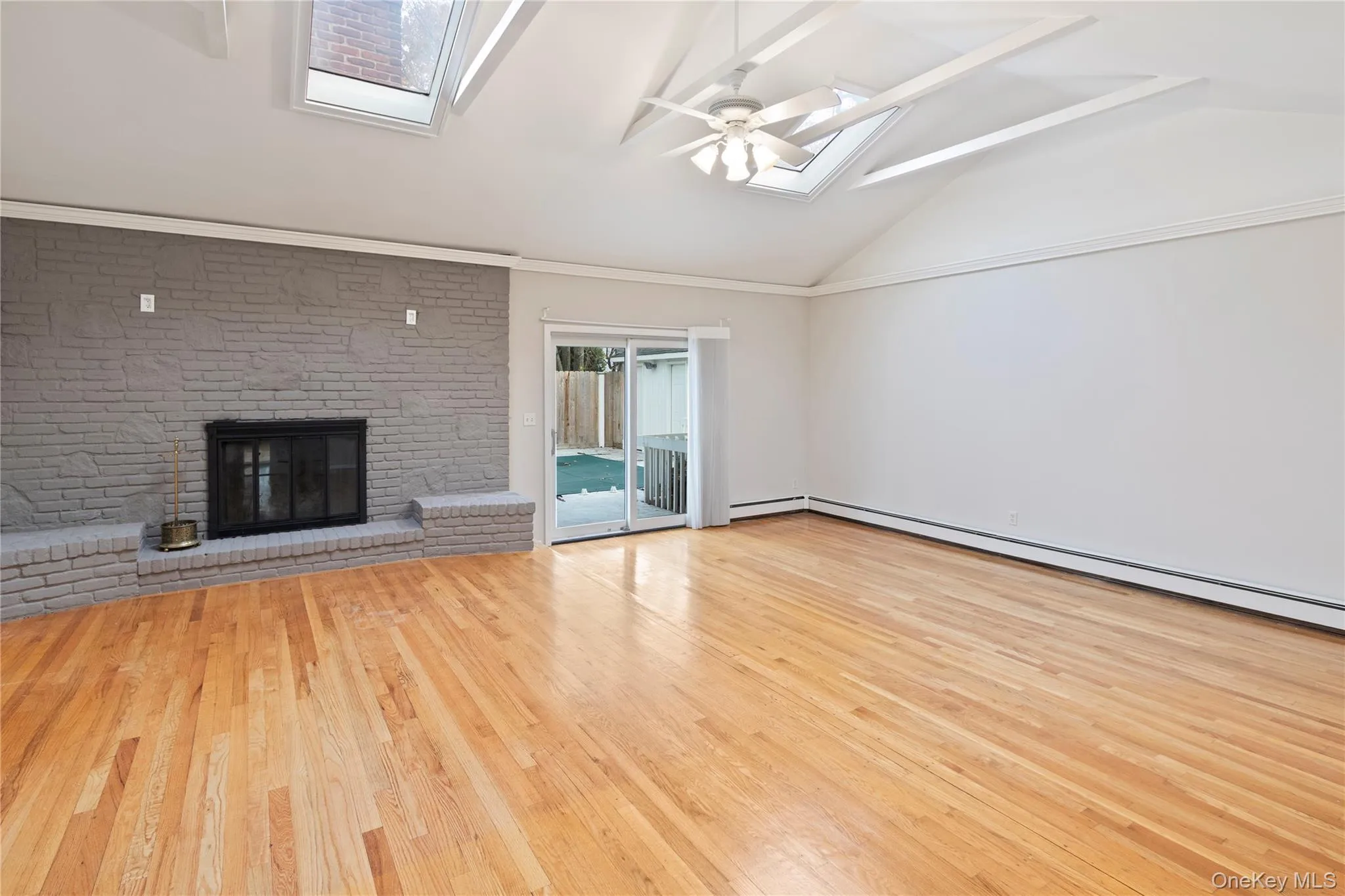 Unfurnished living room with a skylight, vaulted ceiling, a ceiling fan, wood finished floors, and a fireplace Unfurnished living room with a skylight, vaulted ceiling, a ceiling fan, wood finished floors, and a fireplace