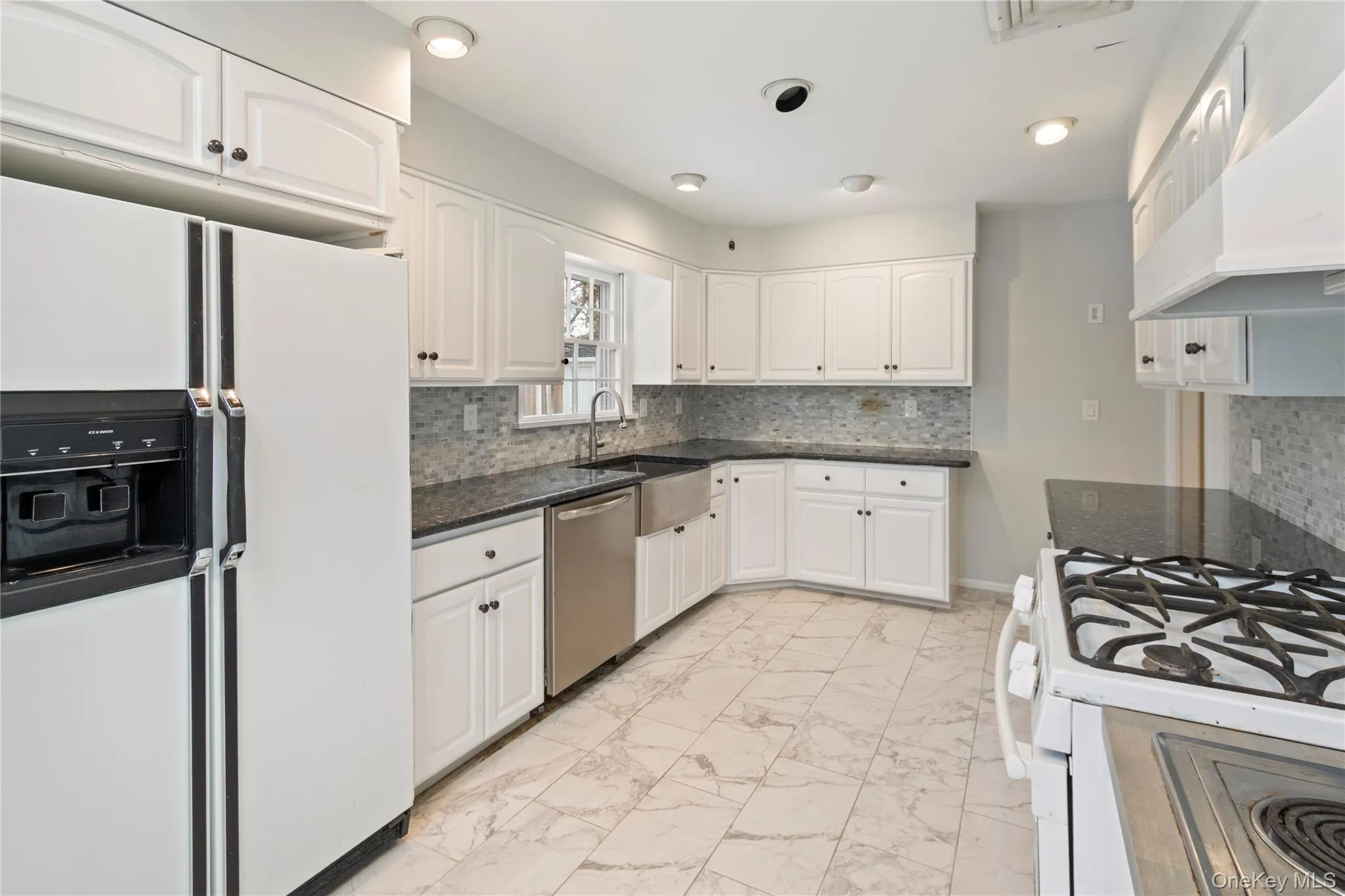 Kitchen featuring white appliances, backsplash, light marble finish floors, white cabinets, and under cabinet range hood Kitchen featuring white appliances, backsplash, light marble finish floors, white cabinets, and under cabinet range hood