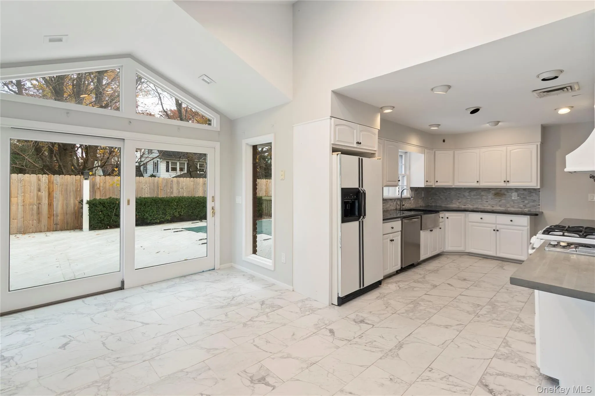 Kitchen with light marble finish floors, white cabinets, white refrigerator with ice dispenser, dark countertops, and high vaulted ceiling Kitchen with light marble finish floors, white cabinets, white refrigerator with ice dispenser, dark countertops, and high vaulted ceiling