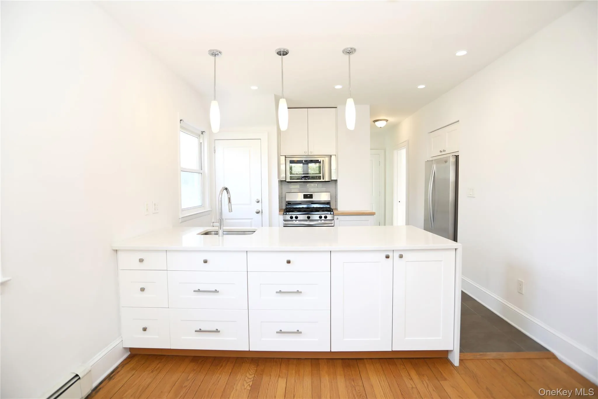 Kitchen with a peninsula, stainless steel appliances, hanging light fixtures, white cabinets, and a baseboard heating unit Kitchen with a peninsula, stainless steel appliances, hanging light fixtures, white cabinets, and a baseboard heating unit
