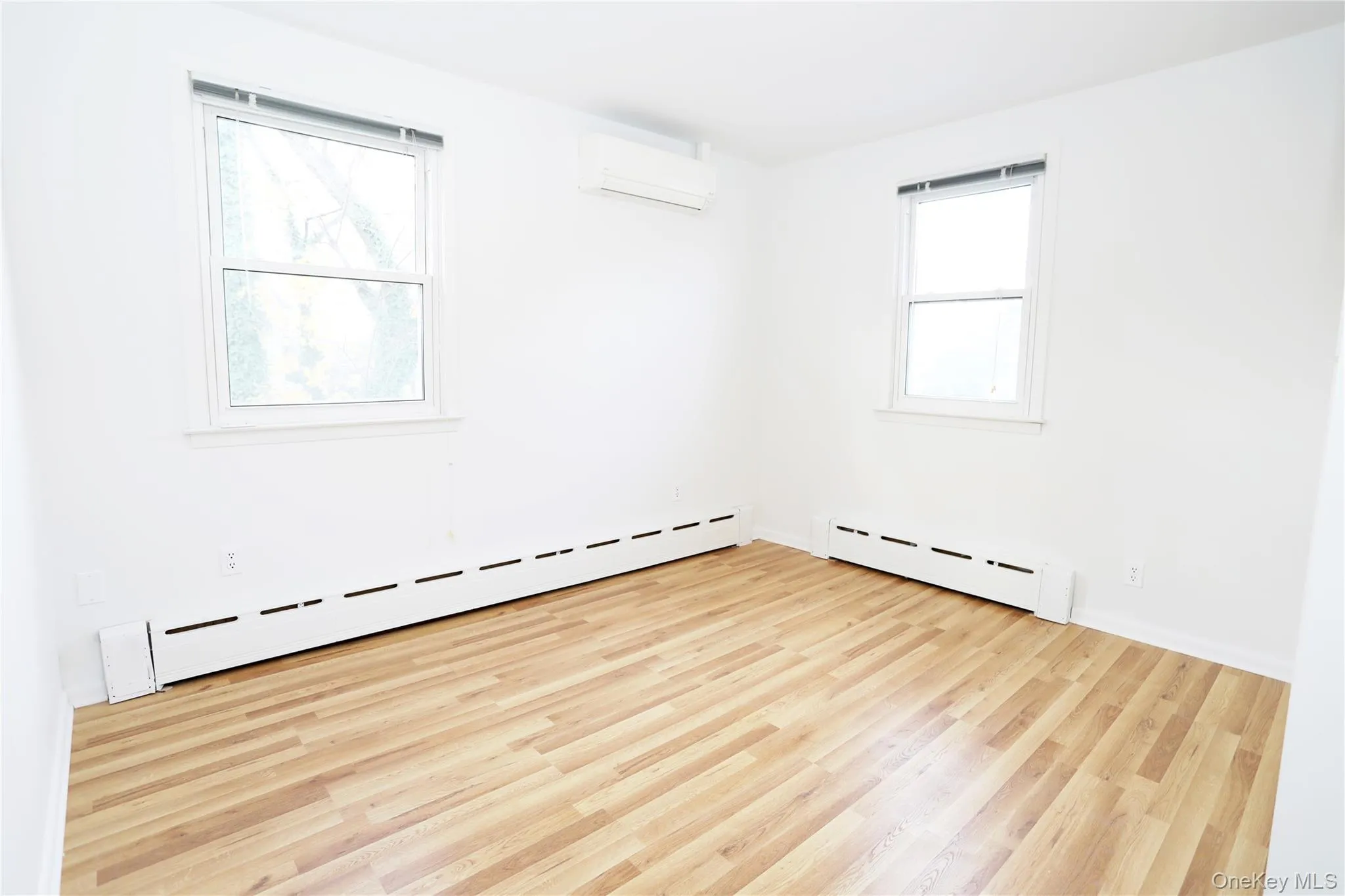 Empty room featuring a baseboard heating unit, light wood-style floors, and a wall mounted AC Empty room featuring a baseboard heating unit, light wood-style floors, and a wall mounted AC