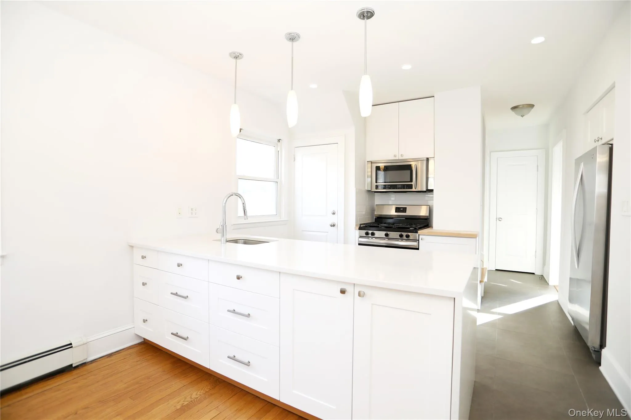 Kitchen with white cabinets, stainless steel appliances, a peninsula, a baseboard heating unit, and pendant lighting Kitchen with white cabinets, stainless steel appliances, a peninsula, a baseboard heating unit, and pendant lighting
