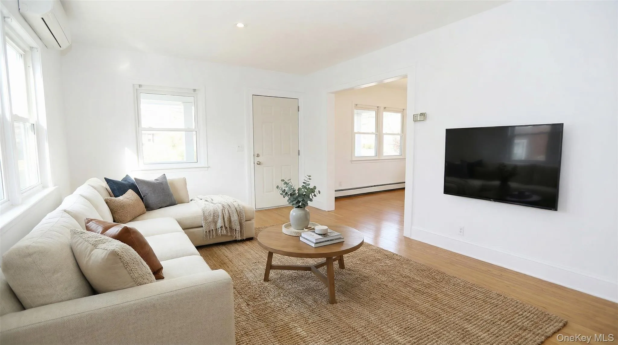 Living room featuring a wall mounted air conditioner, wood finished floors, and a baseboard heating unit Living room featuring a wall mounted air conditioner, wood finished floors, and a baseboard heating unit