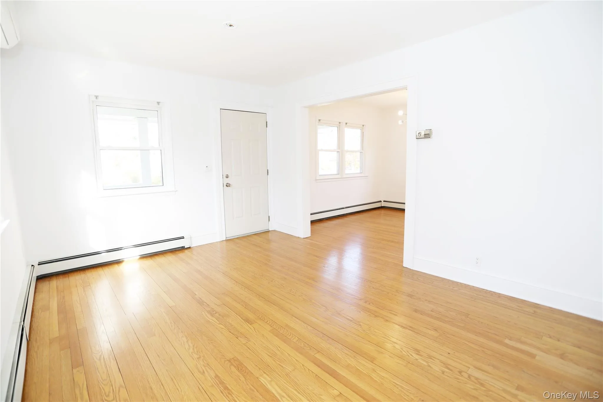 Empty room featuring a baseboard heating unit, a wall mounted air conditioner, and light wood-type flooring Empty room featuring a baseboard heating unit, a wall mounted air conditioner, and light wood-type flooring