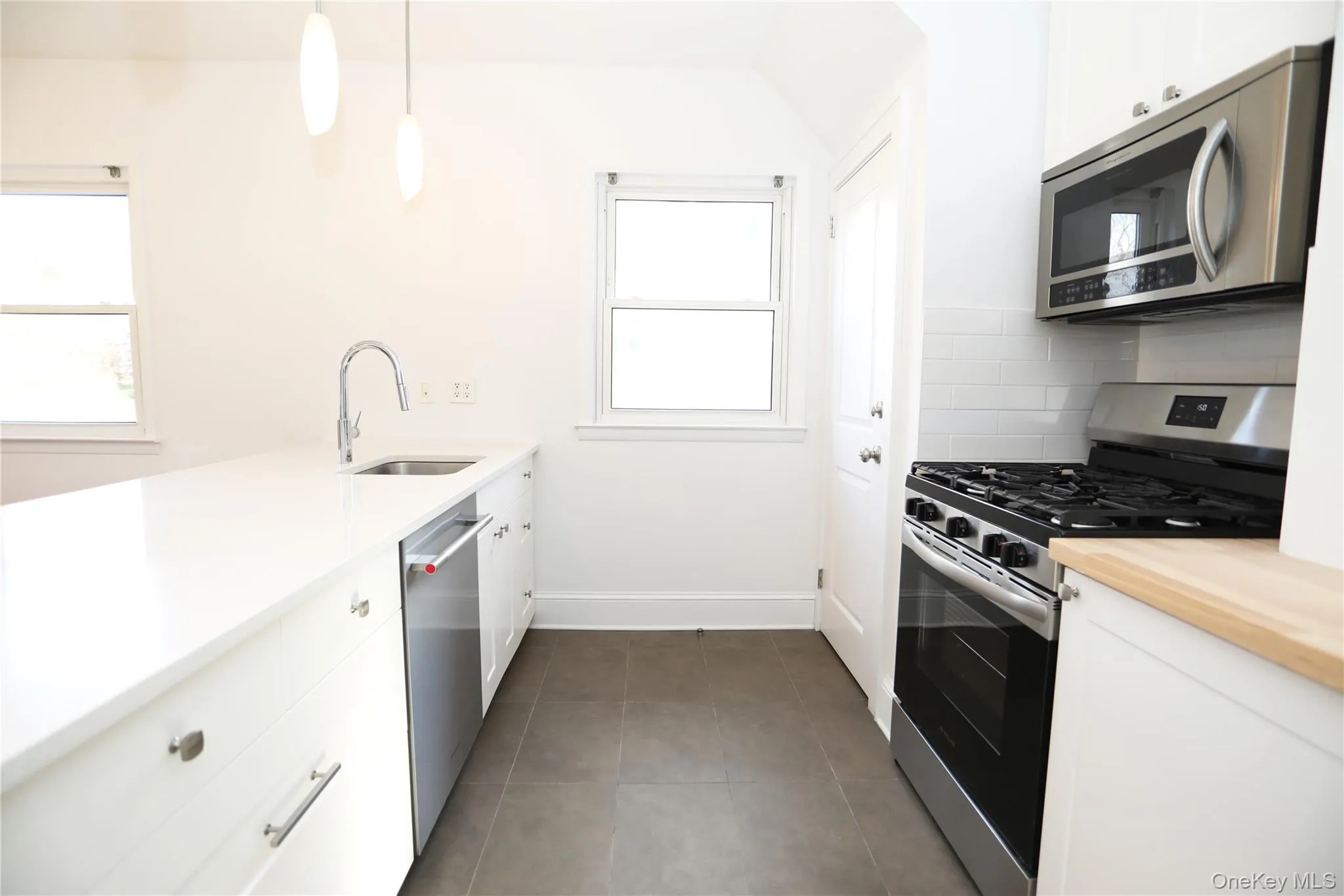 Kitchen featuring appliances with stainless steel finishes, hanging light fixtures, white cabinetry, and a peninsula Kitchen featuring appliances with stainless steel finishes, hanging light fixtures, white cabinetry, and a peninsula
