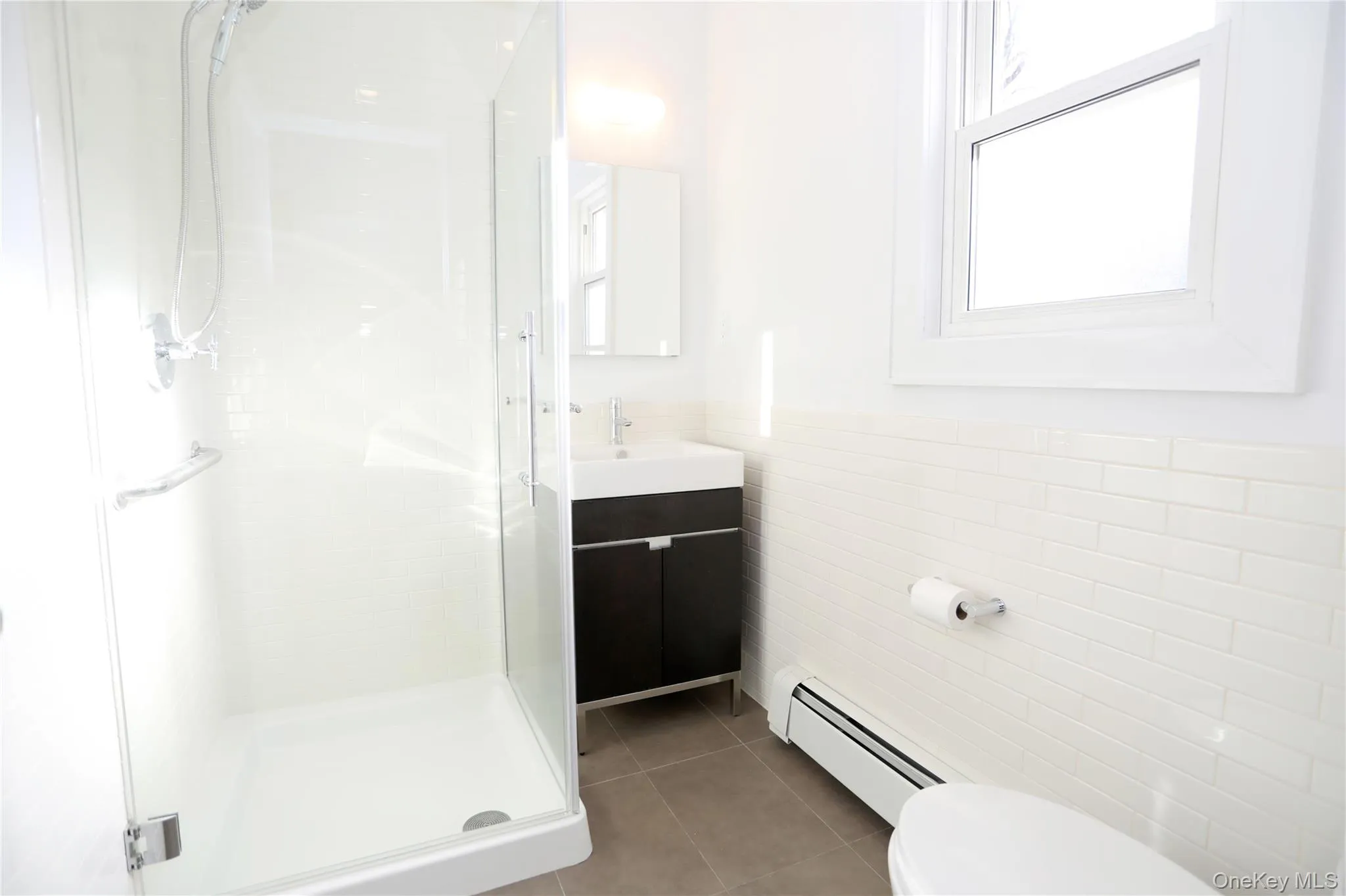 Full bathroom featuring a stall shower, baseboard heating, vanity, light tile patterned floors, and tile walls Full bathroom featuring a stall shower, baseboard heating, vanity, light tile patterned floors, and tile walls