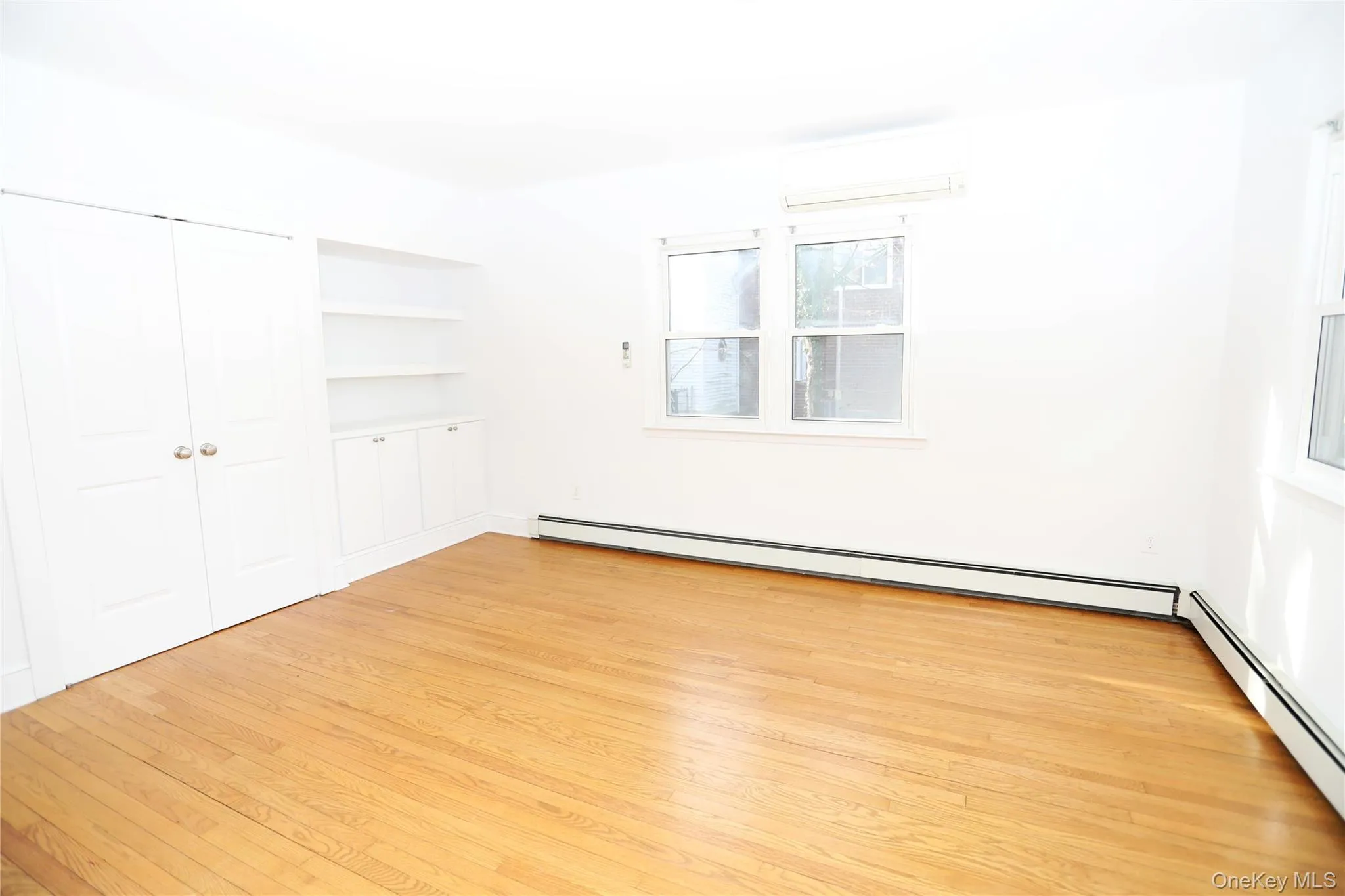 Unfurnished bedroom with a baseboard radiator, light wood-style floors, a wall unit AC, and a closet Unfurnished bedroom with a baseboard radiator, light wood-style floors, a wall unit AC, and a closet