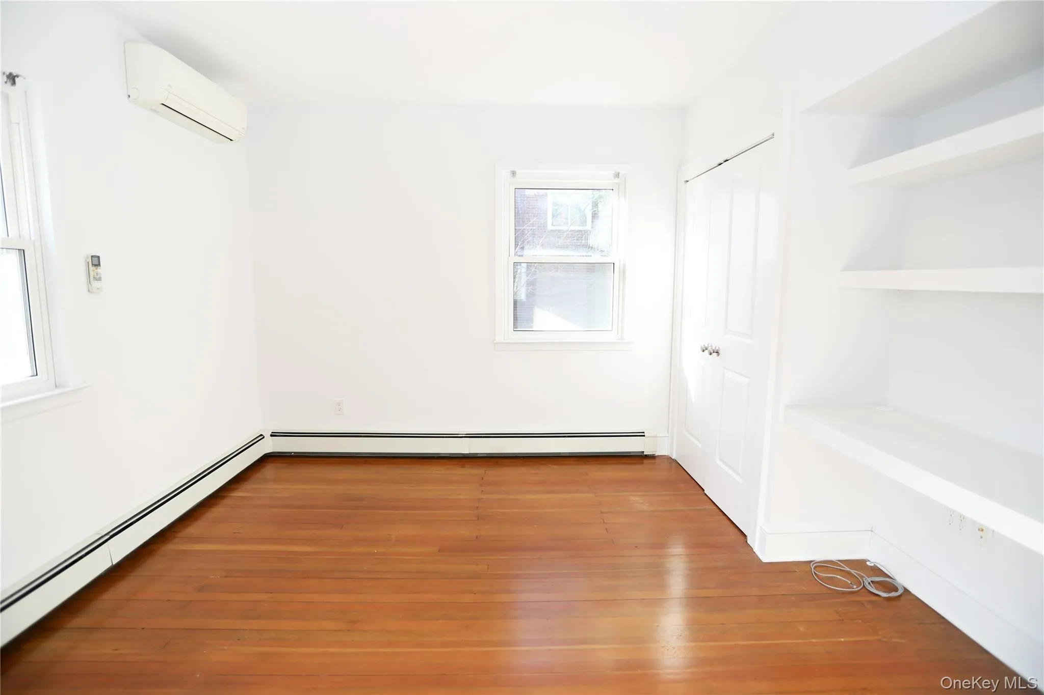 Unfurnished room featuring baseboard heating, a wall unit AC, and wood-type flooring Unfurnished room featuring baseboard heating, a wall unit AC, and wood-type flooring