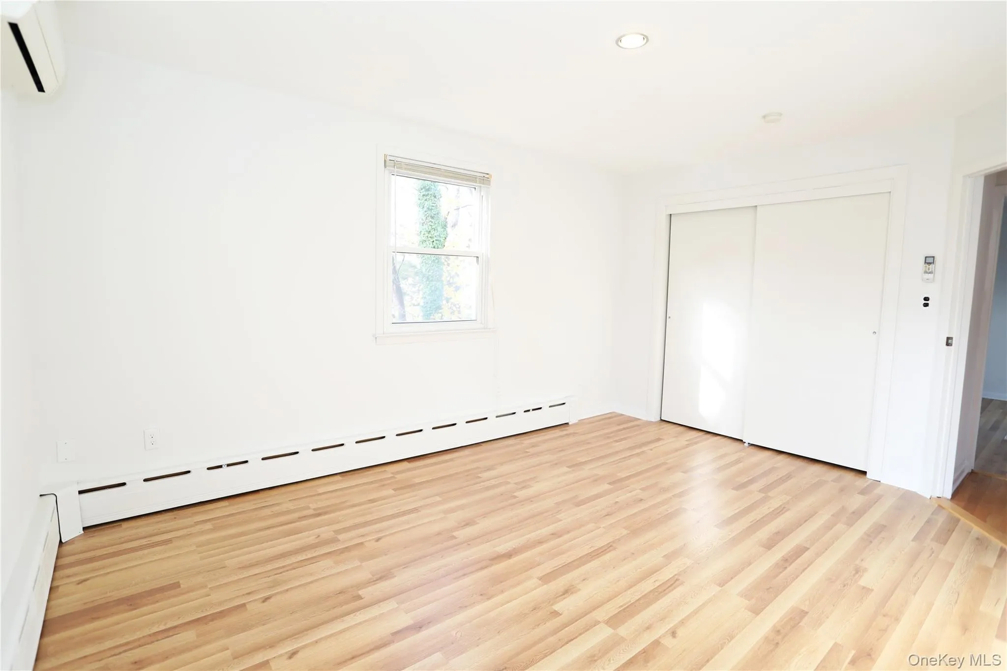 Unfurnished bedroom featuring baseboard heating, a wall unit AC, light wood-style floors, a closet, and recessed lighting Unfurnished bedroom featuring baseboard heating, a wall unit AC, light wood-style floors, a closet, and recessed lighting