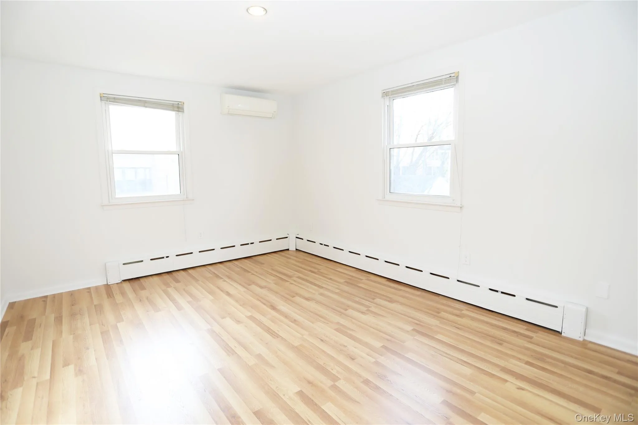 Spare room featuring light wood-type flooring, a wall mounted air conditioner, baseboard heating, plenty of natural light, and recessed lighting Spare room featuring light wood-type flooring, a wall mounted air conditioner, baseboard heating, plenty of natural light, and recessed lighting