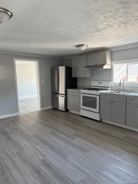 Kitchen with gas range gas stove, light wood finished floors, gray cabinets, freestanding refrigerator, and a textured ceiling Kitchen with gas range gas stove, light wood finished floors, gray cabinets, freestanding refrigerator, and a textured ceiling
