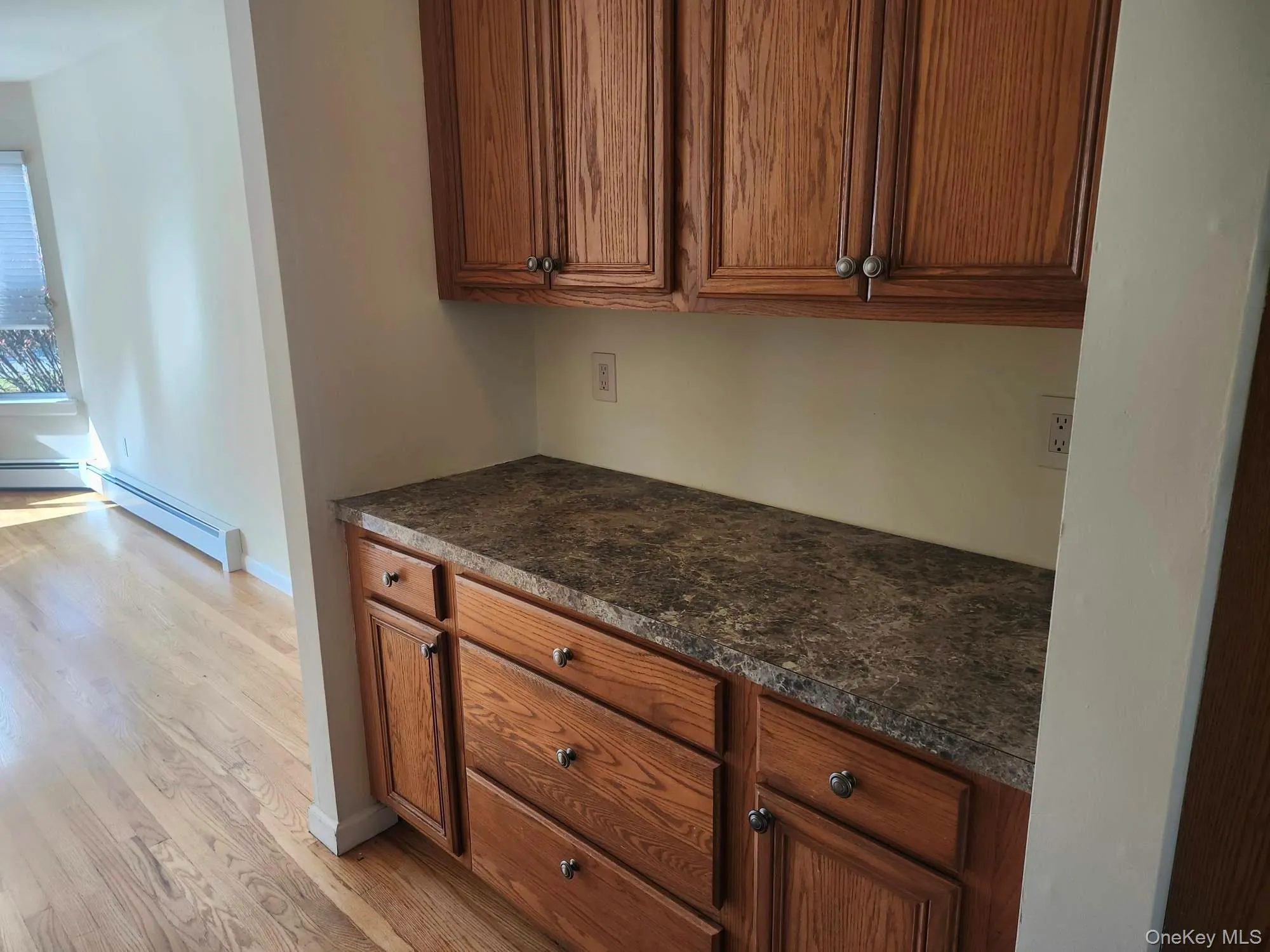 Kitchen with a baseboard radiator, light wood-style flooring, brown cabinetry, and dark countertops Kitchen with a baseboard radiator, light wood-style flooring, brown cabinetry, and dark countertops