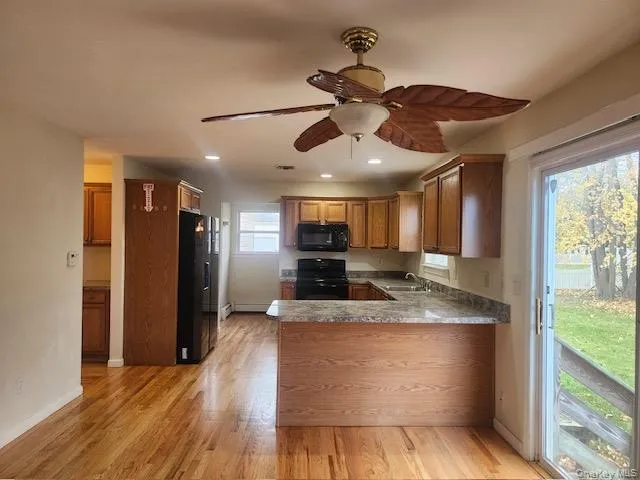 Kitchen with black appliances, a peninsula, light wood finished floors, a ceiling fan, and brown cabinets Kitchen with black appliances, a peninsula, light wood finished floors, a ceiling fan, and brown cabinets