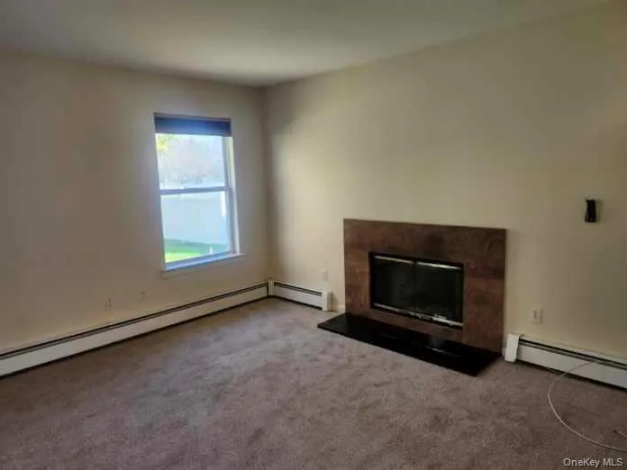 Unfurnished living room featuring a premium fireplace, carpet floors, and baseboard heating Unfurnished living room featuring a premium fireplace, carpet floors, and baseboard heating
