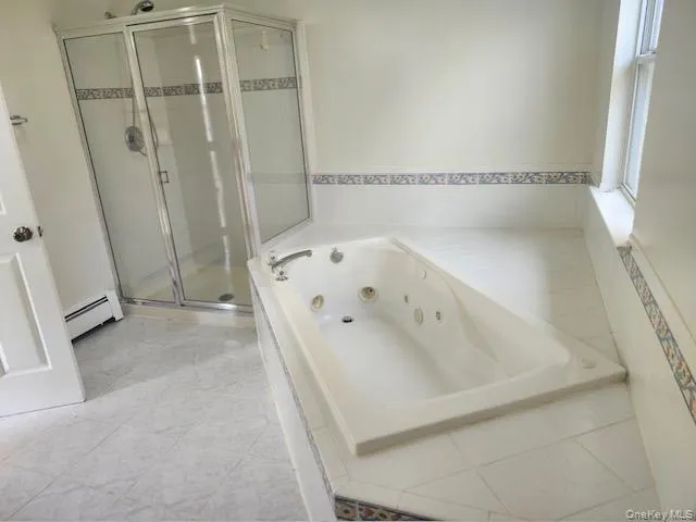 Bathroom with a whirlpool tub, a shower stall, and a baseboard heating unit Bathroom with a whirlpool tub, a shower stall, and a baseboard heating unit