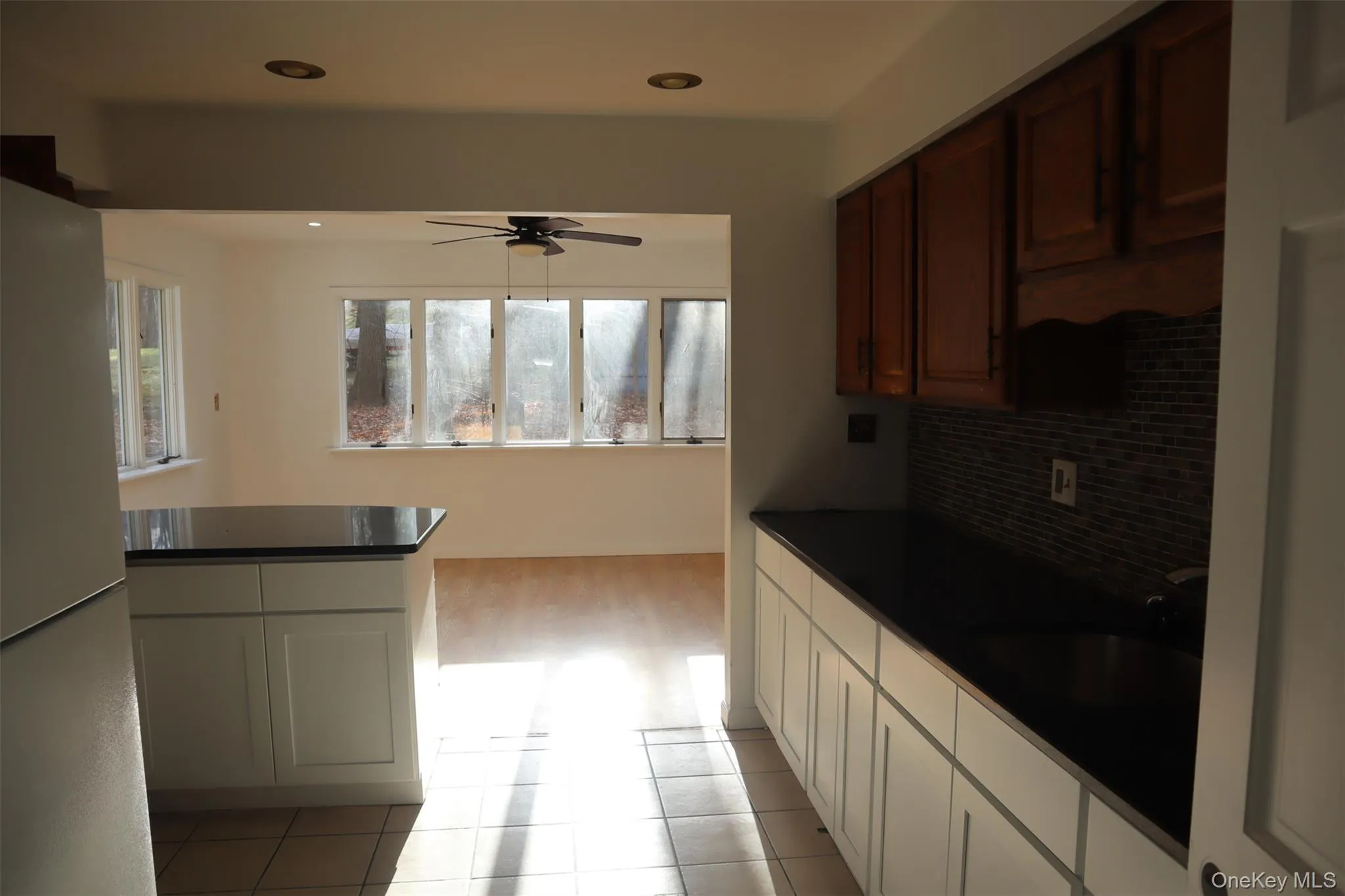 Kitchen featuring dark countertops, freestanding refrigerator, a ceiling fan, light tile patterned floors, and decorative backsplash Kitchen featuring dark countertops, freestanding refrigerator, a ceiling fan, light tile patterned floors, and decorative backsplash
