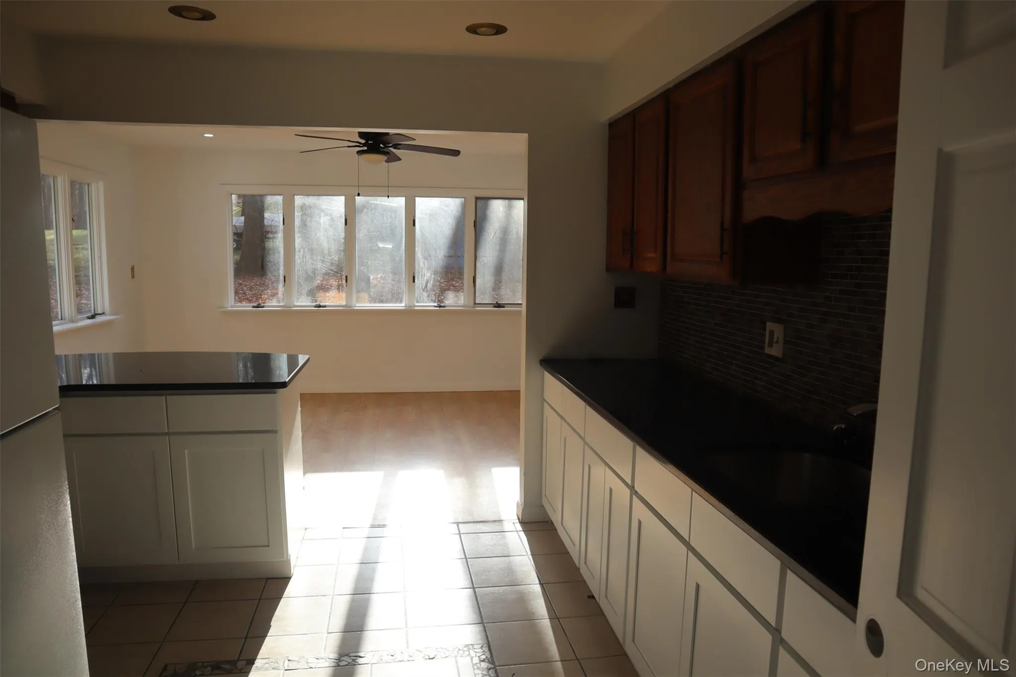 Kitchen with dark countertops, freestanding refrigerator, light tile patterned floors, ceiling fan, and backsplash Kitchen with dark countertops, freestanding refrigerator, light tile patterned floors, ceiling fan, and backsplash