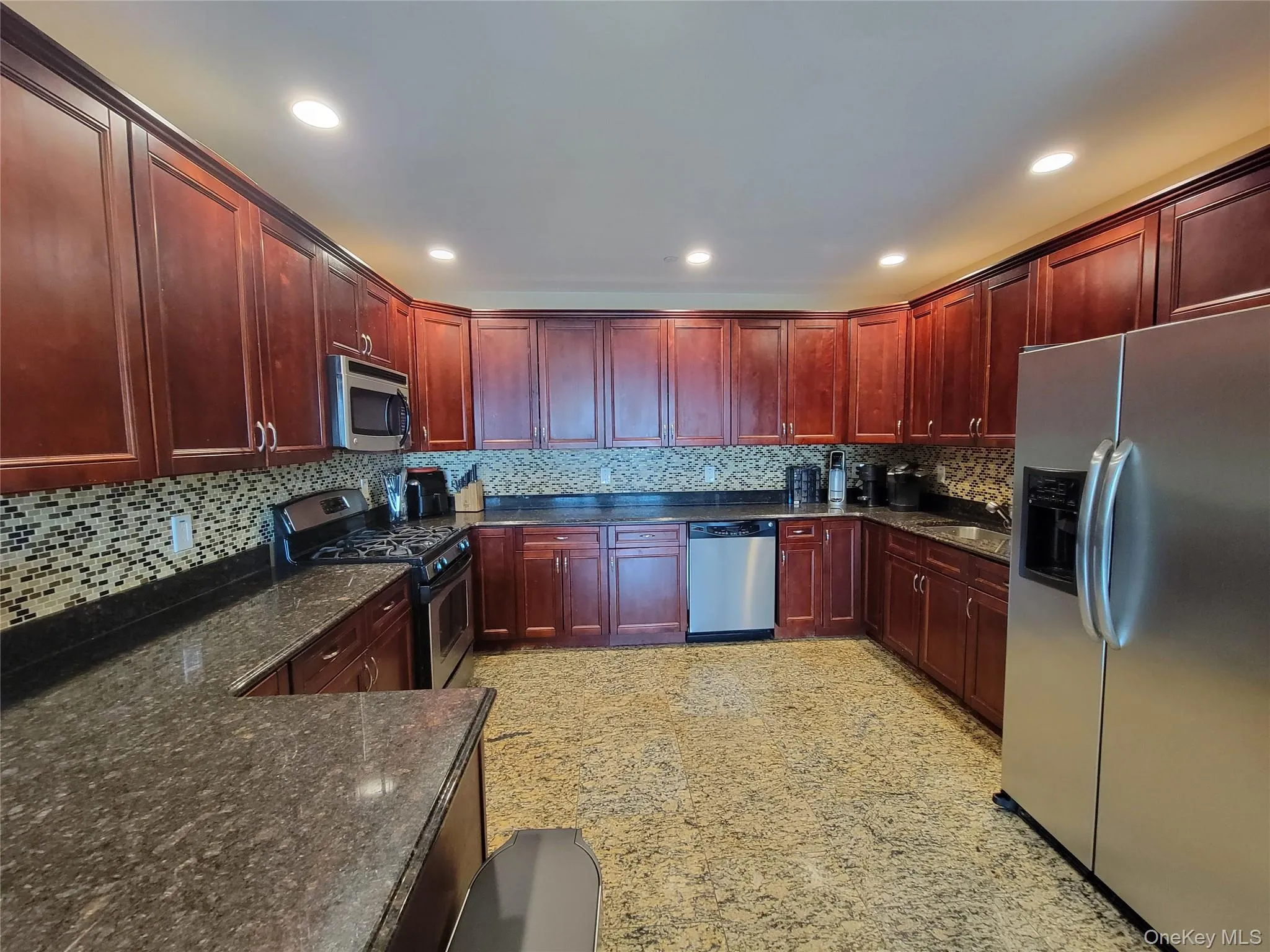 Kitchen featuring dark brown cabinets, appliances with stainless steel finishes, dark stone counters, tasteful backsplash, and recessed lighting Kitchen featuring dark brown cabinets, appliances with stainless steel finishes, dark stone counters, tasteful backsplash, and recessed lighting