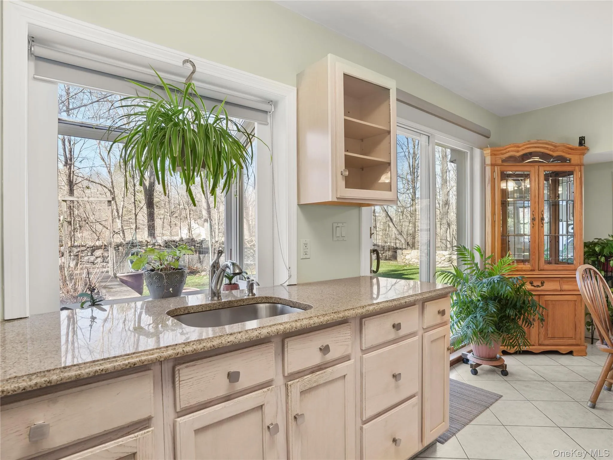Kitchen with light brown cabinets, light stone counters, glass insert cabinets, and light tile patterned flooring Kitchen with light brown cabinets, light stone counters, glass insert cabinets, and light tile patterned flooring