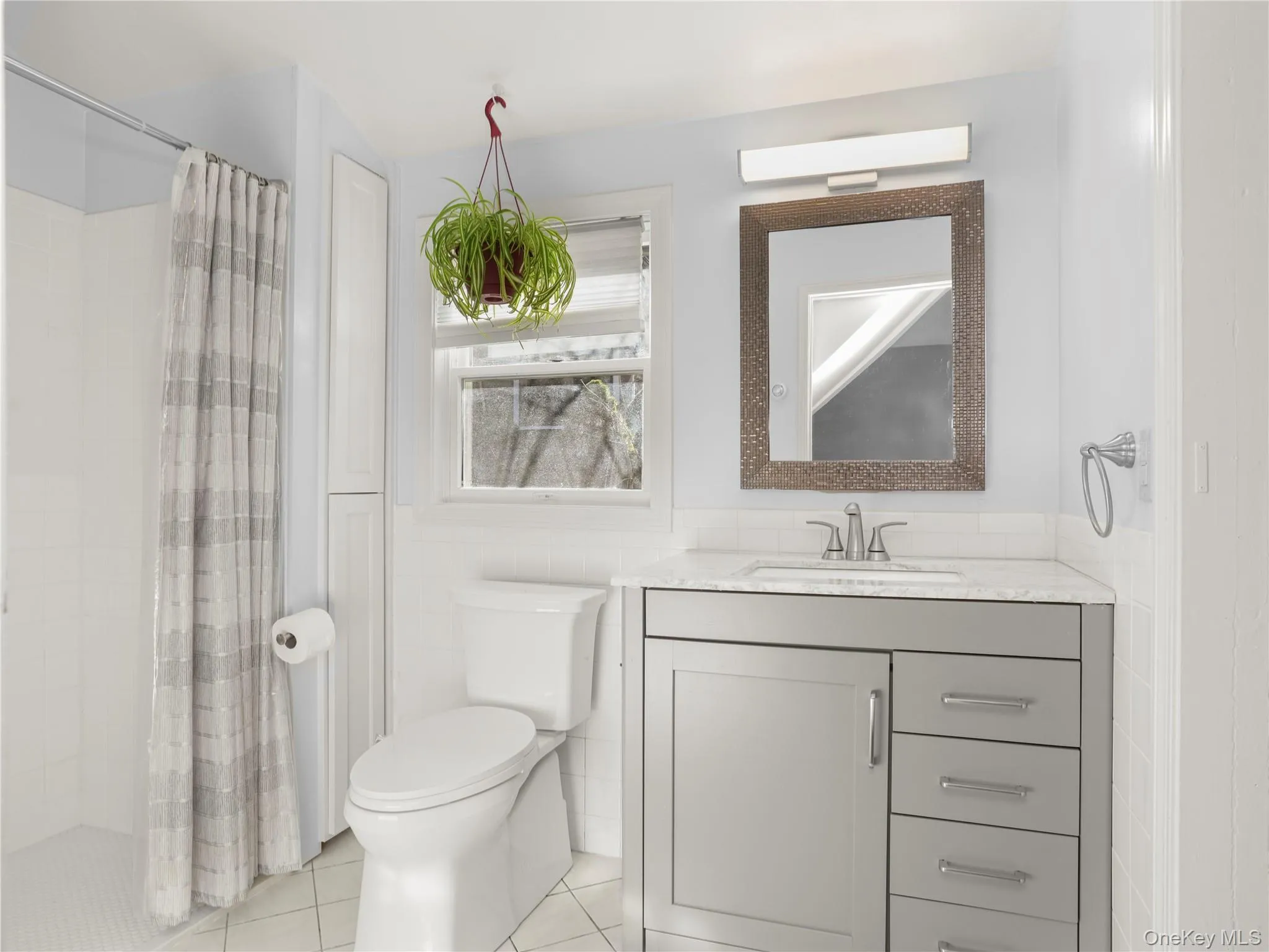 Full bath with tile walls, a stall shower, light tile patterned flooring, vanity, and a wainscoted wall Full bath with tile walls, a stall shower, light tile patterned flooring, vanity, and a wainscoted wall