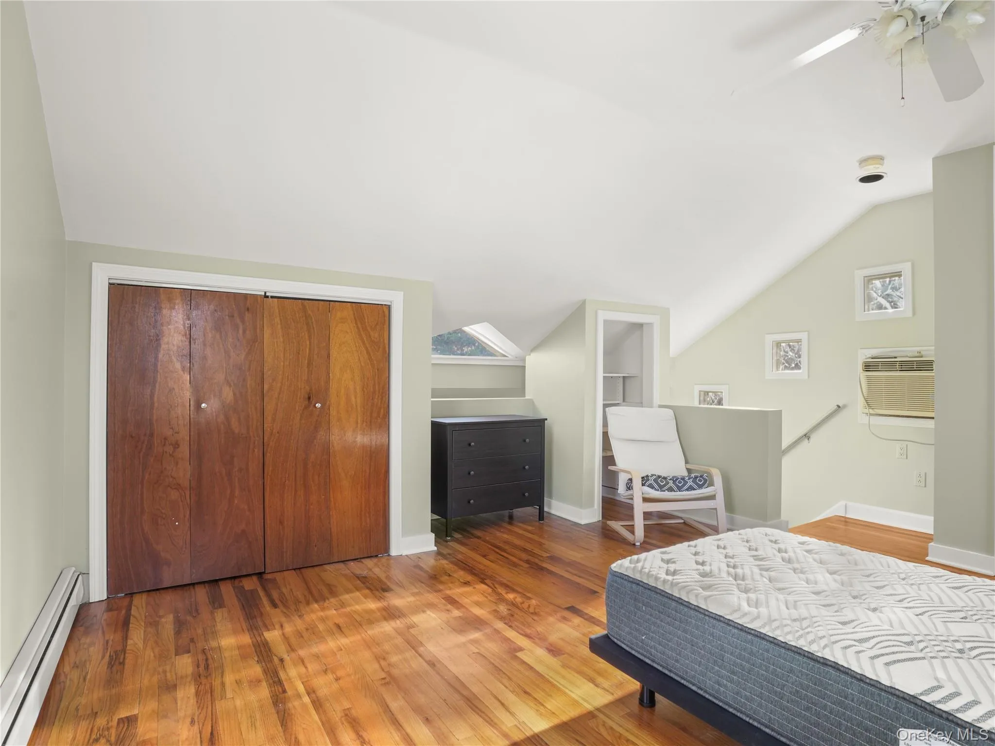 Bedroom with a baseboard radiator, lofted ceiling, wood finished floors, ceiling fan, and a closet Bedroom with a baseboard radiator, lofted ceiling, wood finished floors, ceiling fan, and a closet