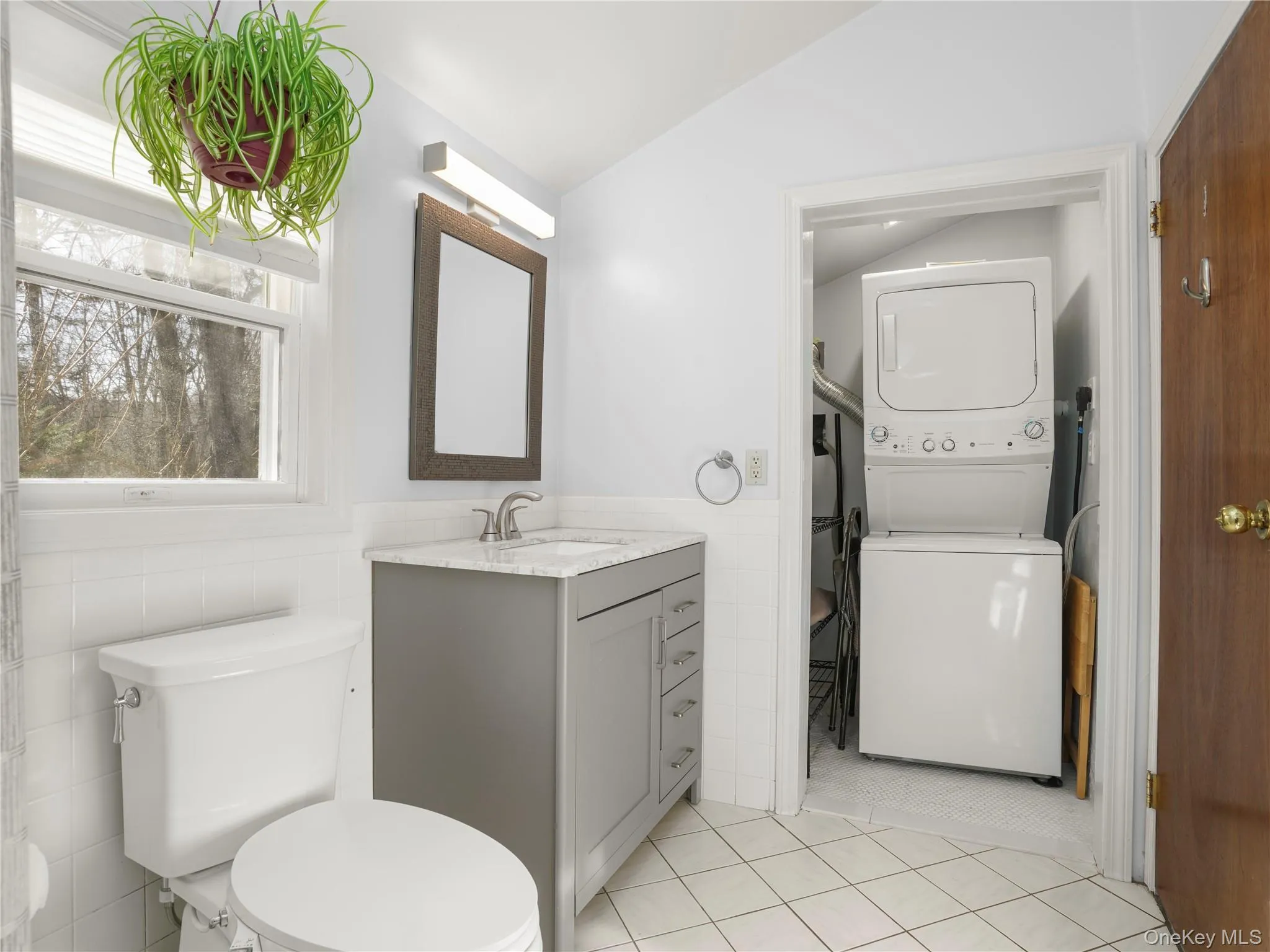 Bathroom featuring light tile patterned floors, tile walls, vanity, stacked washer / drying machine, and wainscoting Bathroom featuring light tile patterned floors, tile walls, vanity, stacked washer / drying machine, and wainscoting