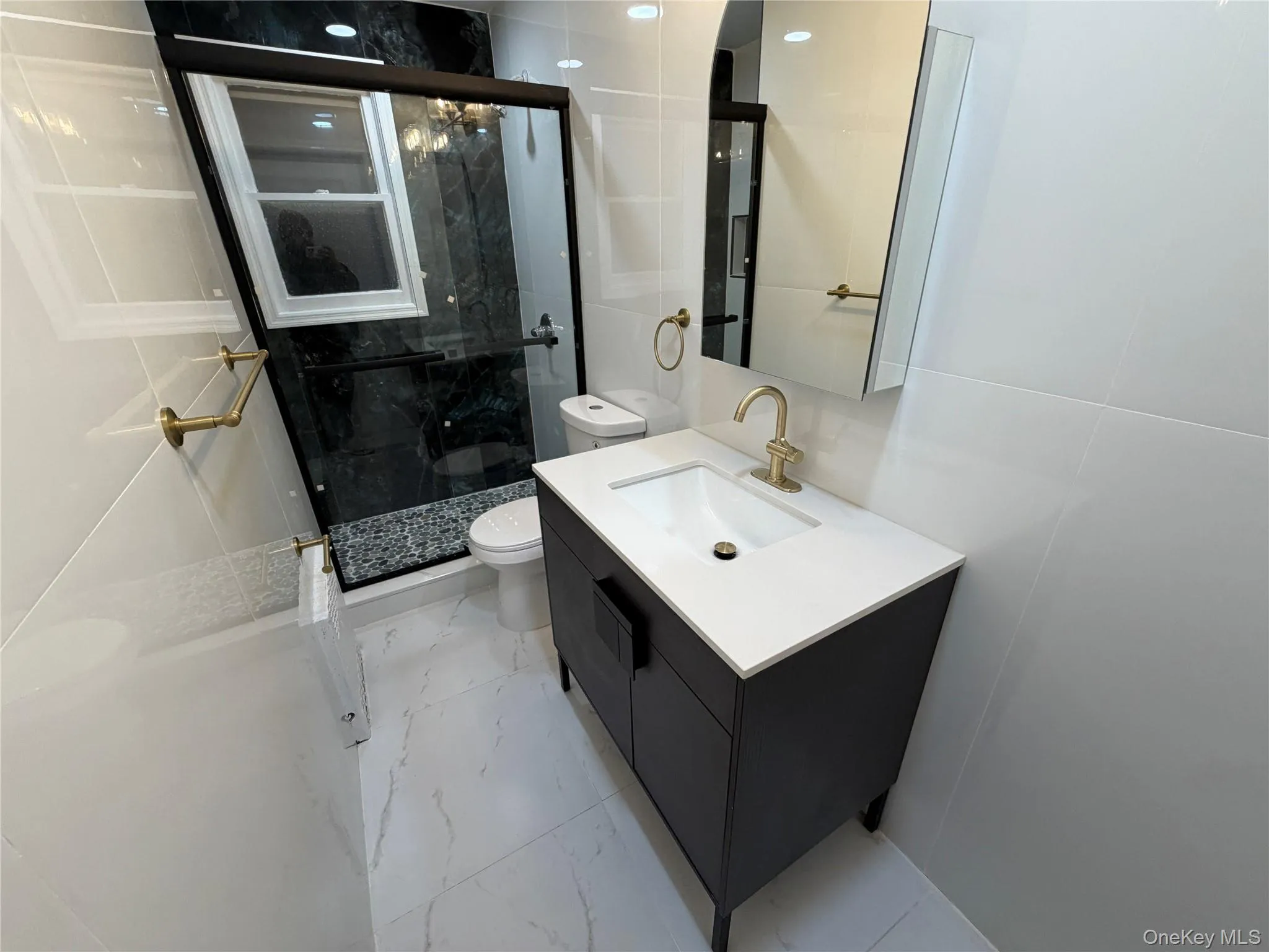Full bath with light marble finish floors, vanity, a marble finish shower, and tile walls Full bath with light marble finish floors, vanity, a marble finish shower, and tile walls