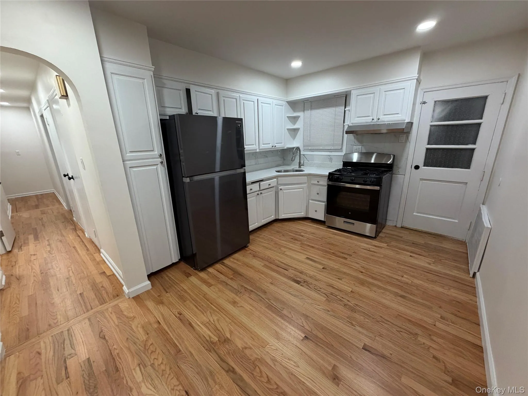 Kitchen with white cabinets, arched walkways, freestanding refrigerator, gas stove, and light countertops Kitchen with white cabinets, arched walkways, freestanding refrigerator, gas stove, and light countertops