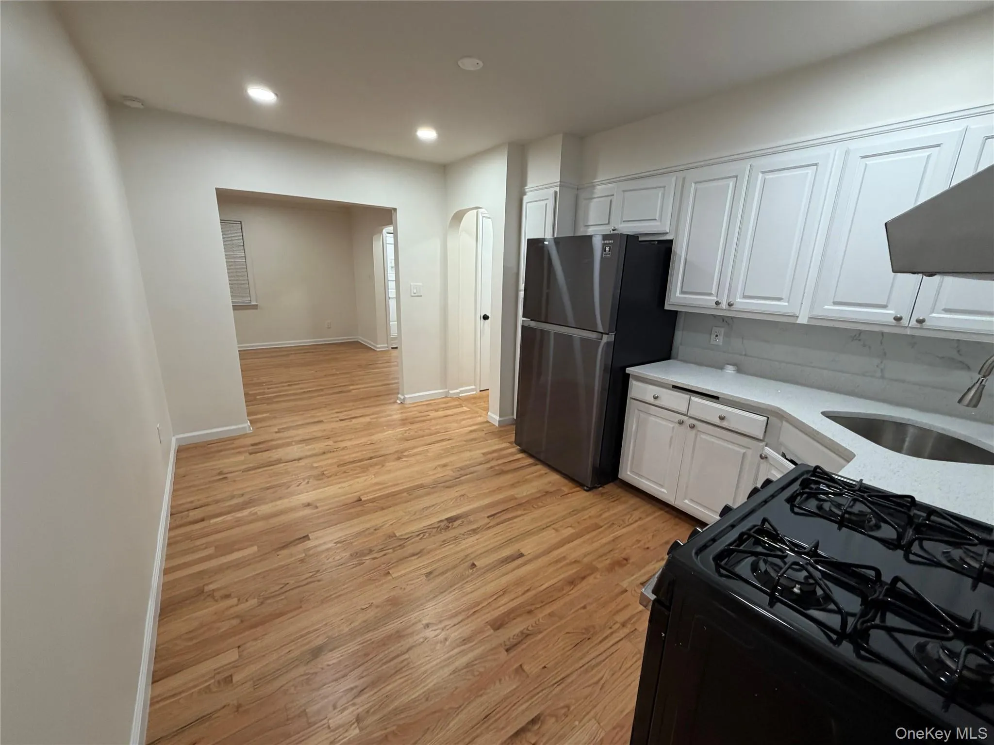 Kitchen with gas stove, white cabinets, light wood finished floors, recessed lighting, and light stone counters Kitchen with gas stove, white cabinets, light wood finished floors, recessed lighting, and light stone counters