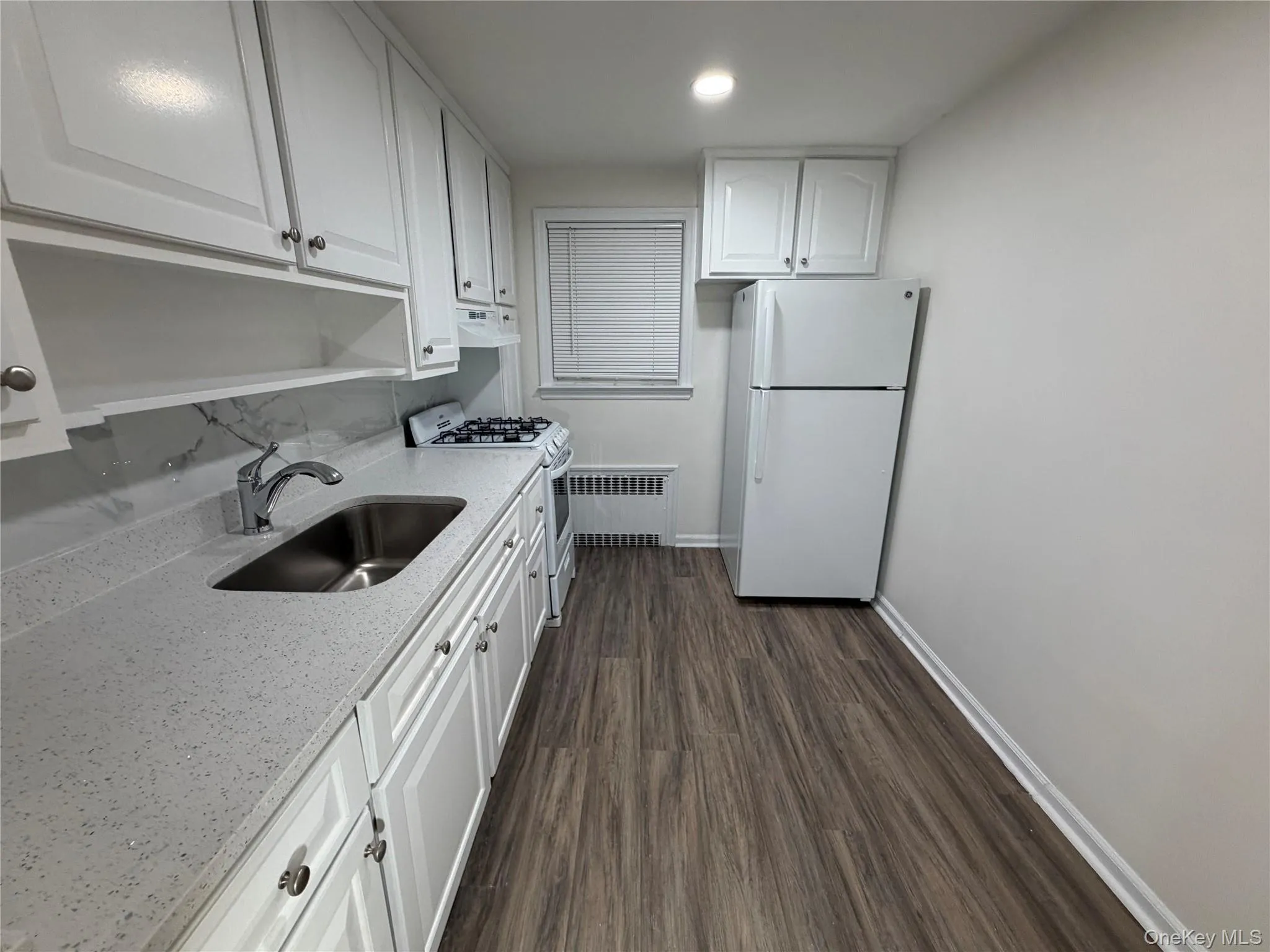 Kitchen featuring radiator heating unit, white appliances, white cabinetry, dark wood-style floors, and recessed lighting Kitchen featuring radiator heating unit, white appliances, white cabinetry, dark wood-style floors, and recessed lighting