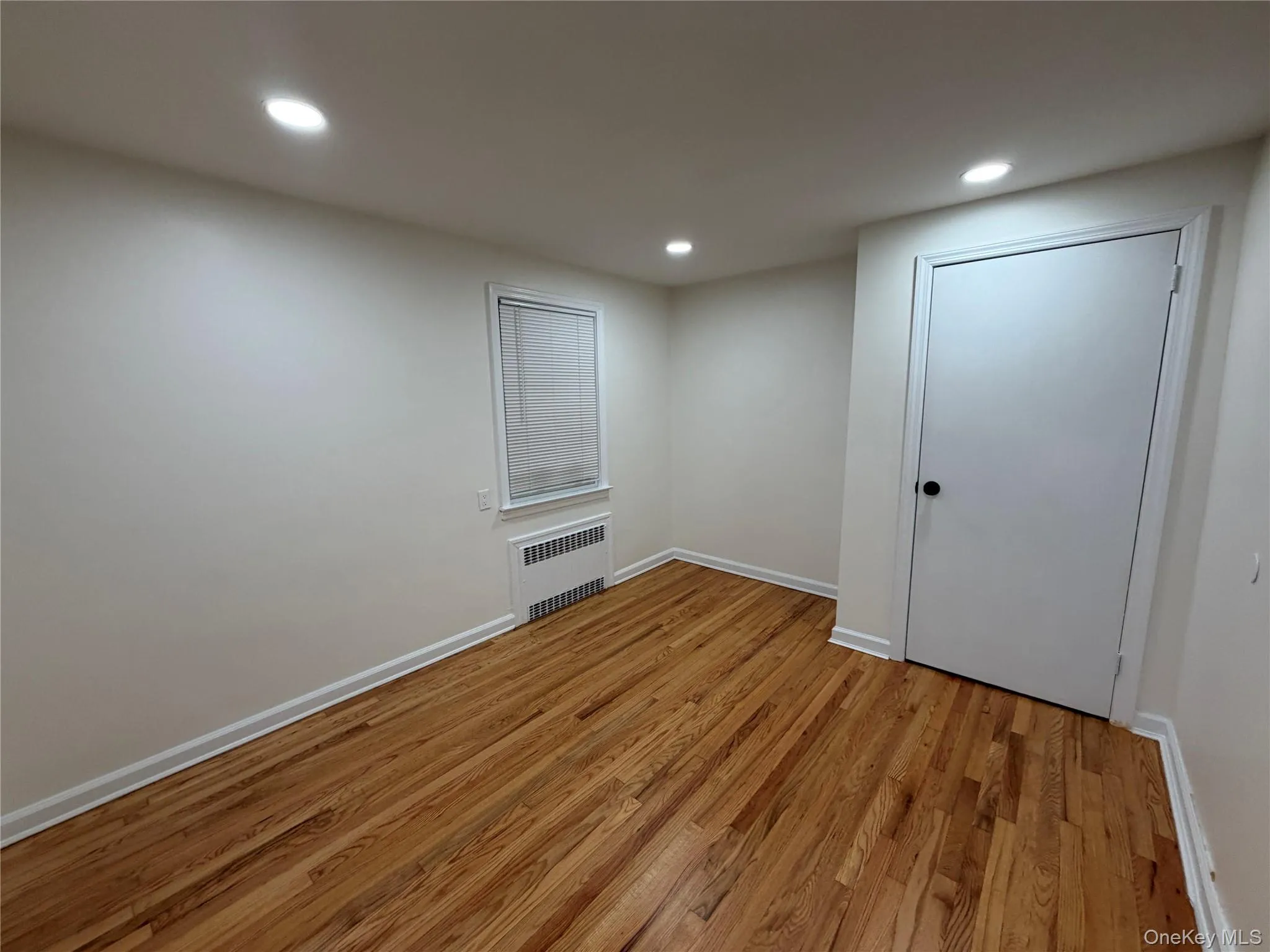 Empty room featuring light wood finished floors, recessed lighting, and radiator Empty room featuring light wood finished floors, recessed lighting, and radiator