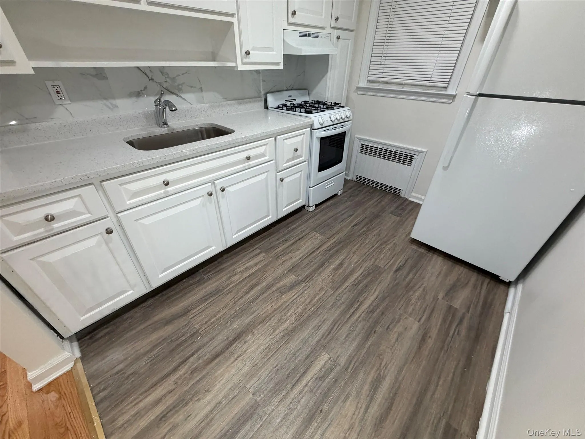 Kitchen featuring white appliances, dark wood-type flooring, white cabinets, light stone countertops, and under cabinet range hood Kitchen featuring white appliances, dark wood-type flooring, white cabinets, light stone countertops, and under cabinet range hood