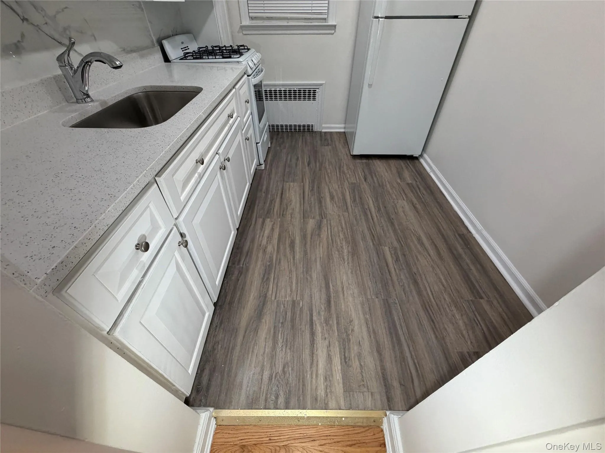 Kitchen featuring white cabinets, white appliances, dark wood finished floors, light stone counters, and radiator Kitchen featuring white cabinets, white appliances, dark wood finished floors, light stone counters, and radiator