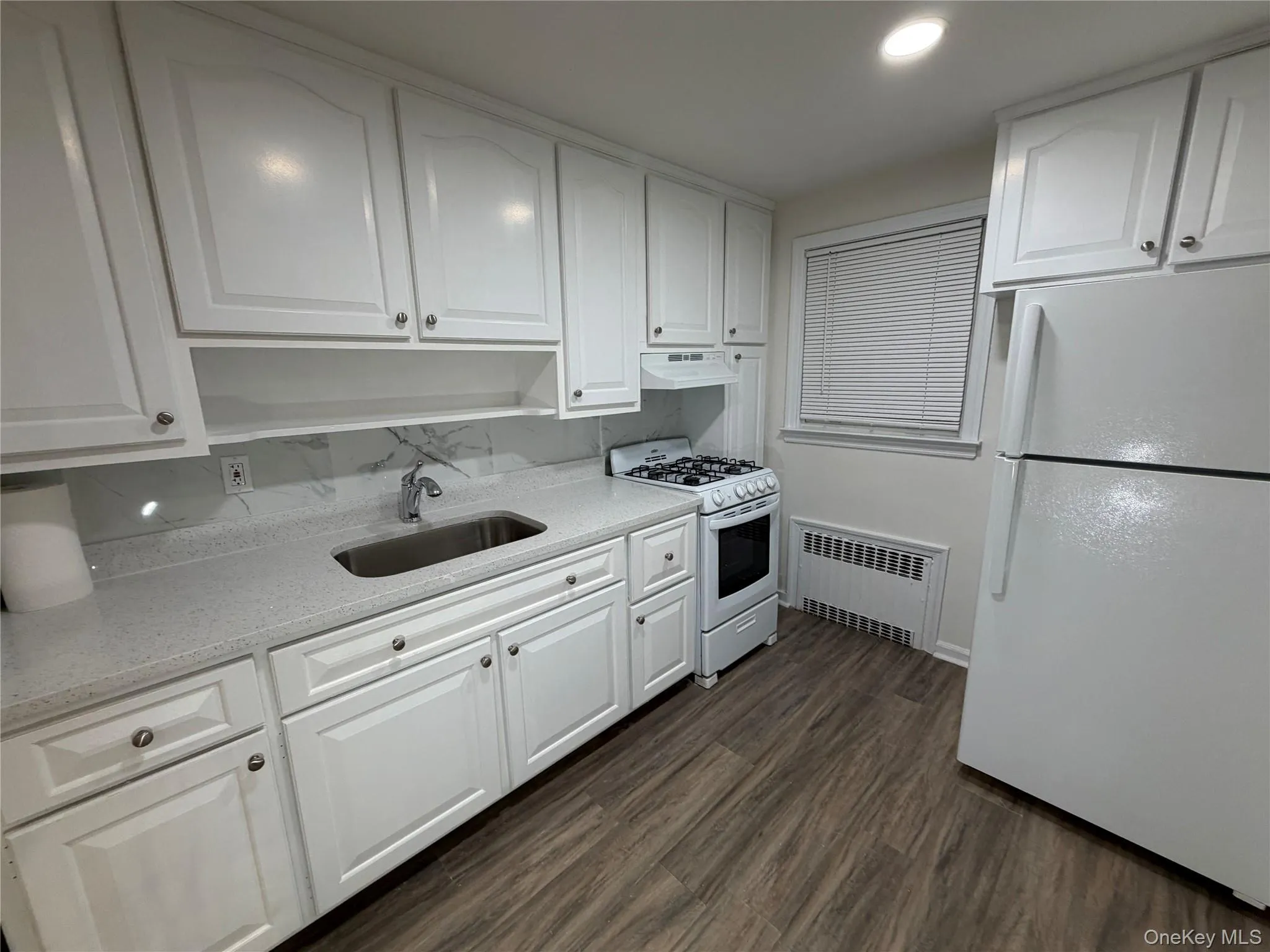 Kitchen with white appliances, white cabinetry, dark wood-style flooring, and recessed lighting Kitchen with white appliances, white cabinetry, dark wood-style flooring, and recessed lighting