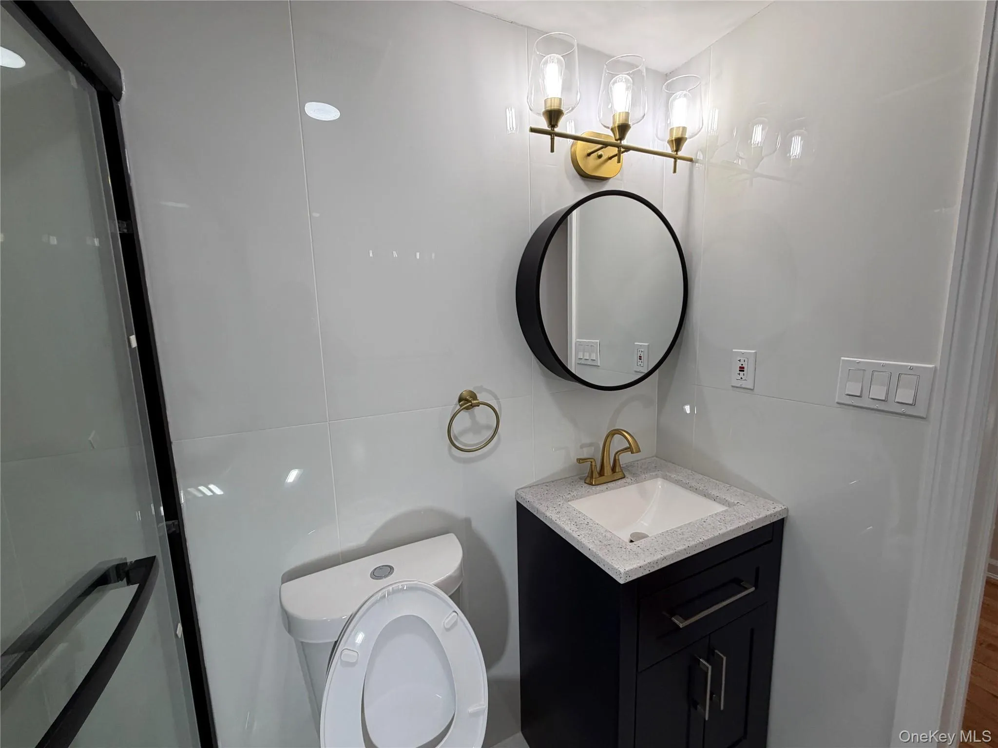 Full bathroom featuring vanity, tile walls, a shower with shower door, and wood finished floors Full bathroom featuring vanity, tile walls, a shower with shower door, and wood finished floors