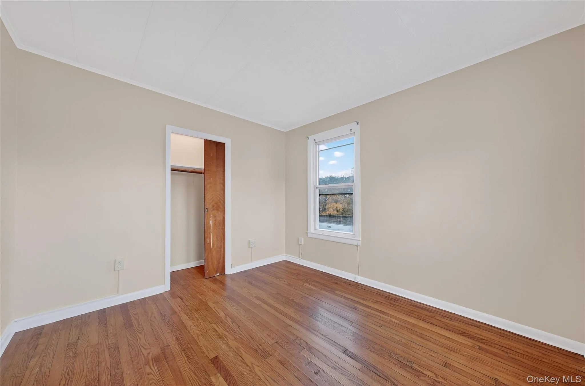 Unfurnished bedroom featuring hardwood / wood-style flooring, ornamental molding, and a closet Unfurnished bedroom featuring hardwood / wood-style flooring, ornamental molding, and a closet