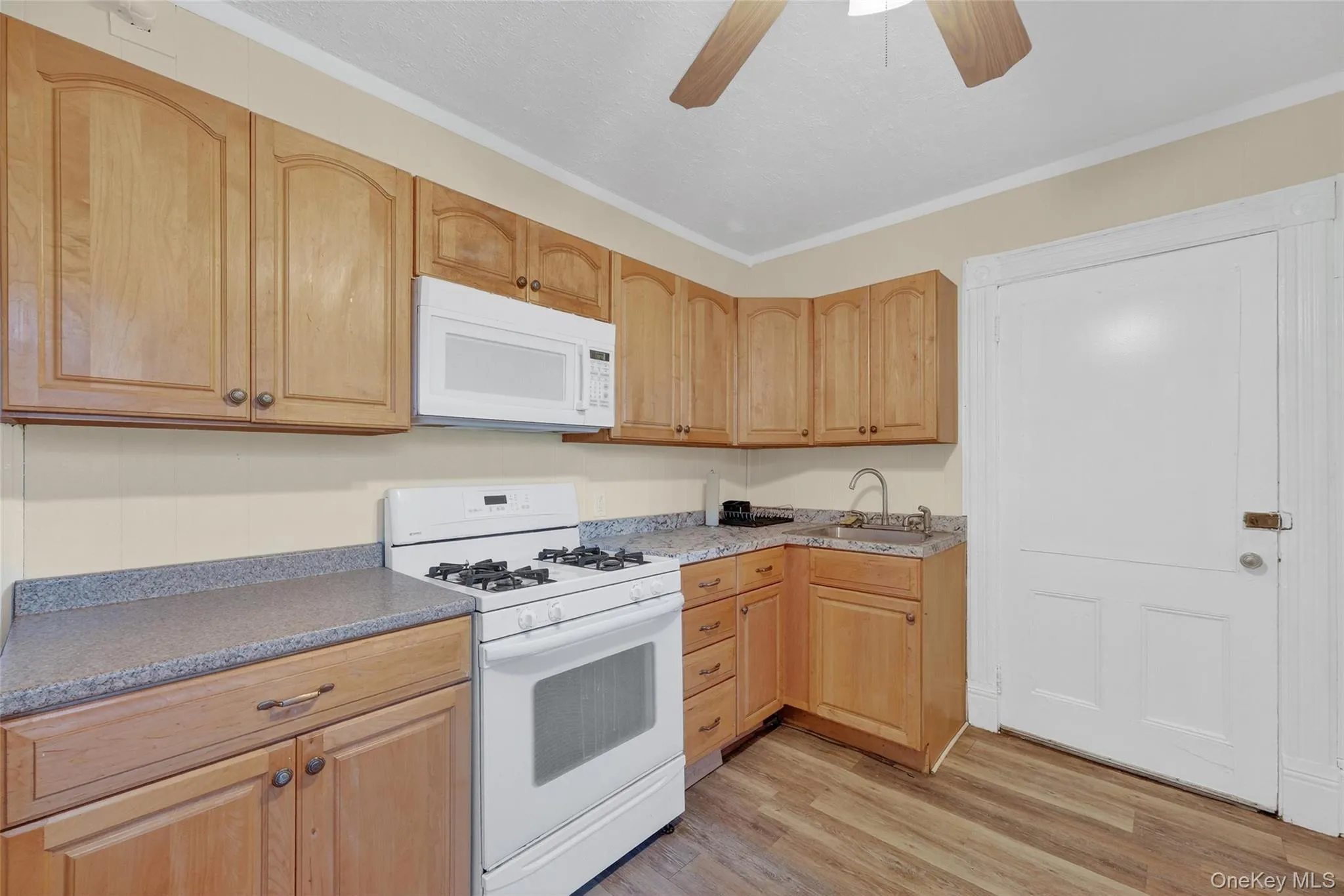 Kitchen featuring white appliances, light wood finished floors, ceiling fan, ornamental molding, and light brown cabinetry Kitchen featuring white appliances, light wood finished floors, ceiling fan, ornamental molding, and light brown cabinetry