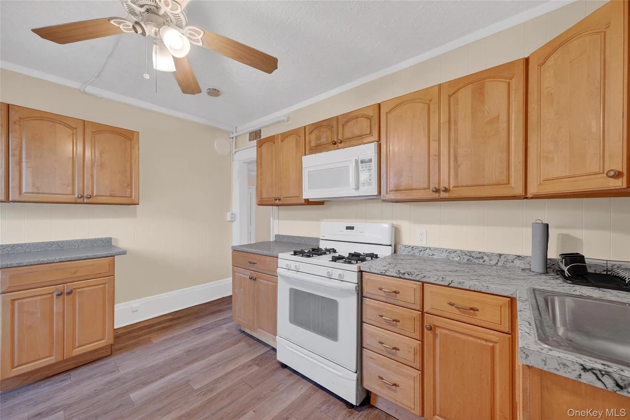 Kitchen featuring white appliances, crown molding, light wood-style flooring, light countertops, and ceiling fan Kitchen featuring white appliances, crown molding, light wood-style flooring, light countertops, and ceiling fan